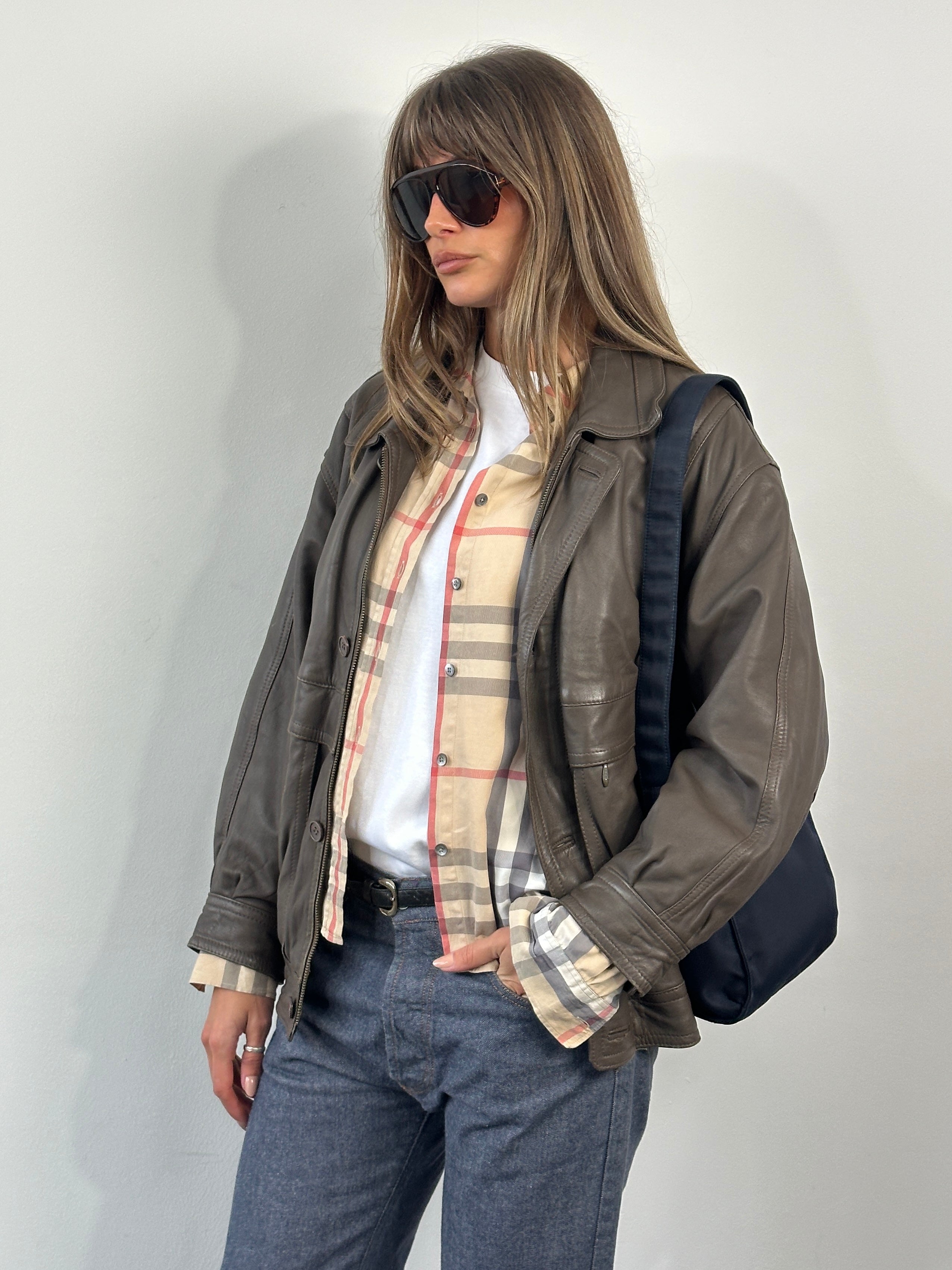 Vintage 1990s leather bomber jacket, size M, with classic design and distressed brown leather, displayed on a hanger.