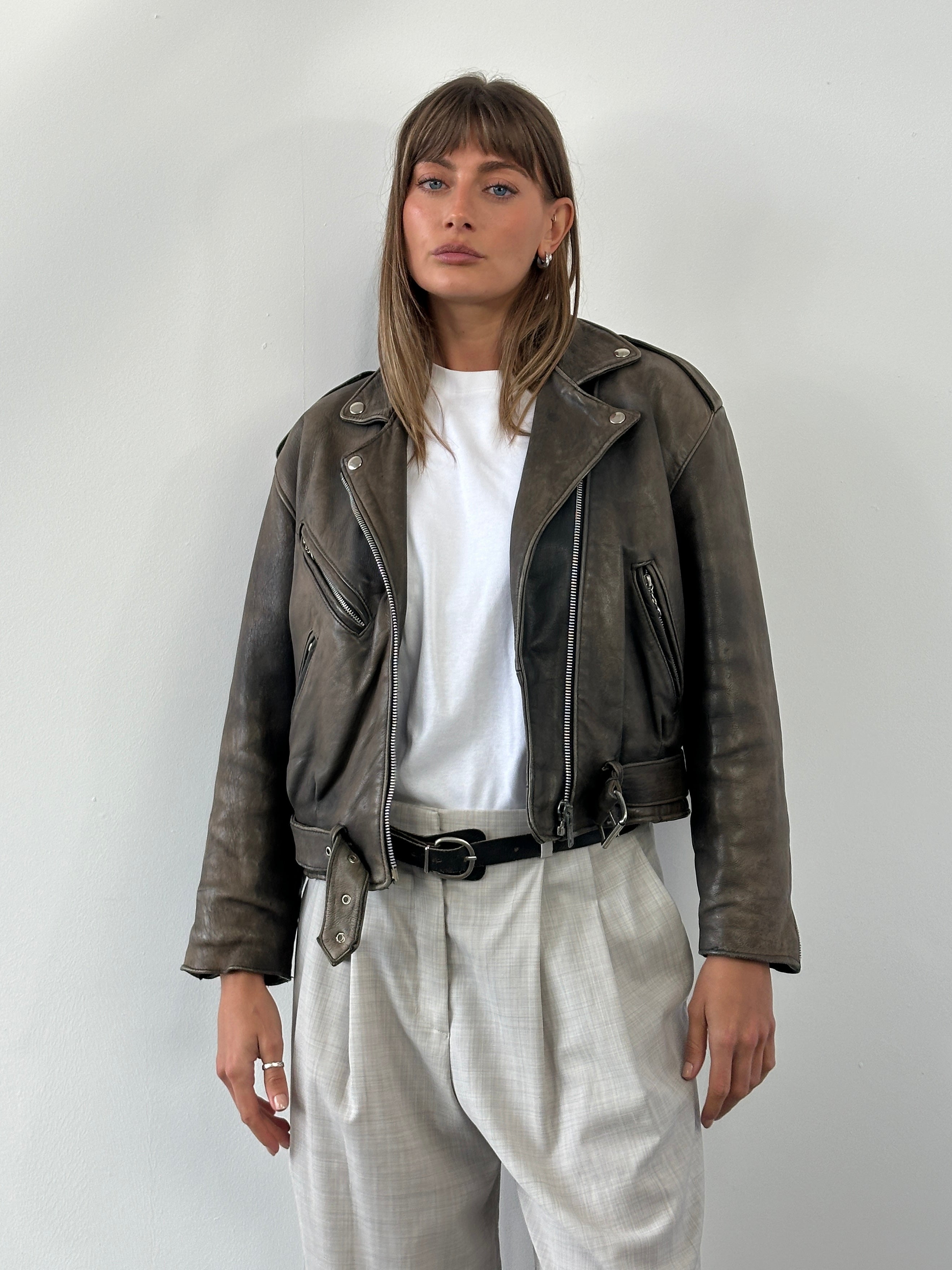 Vintage 1980s distressed leather biker jacket in size small with rugged texture and classic design, featuring metal hardware and worn finish.