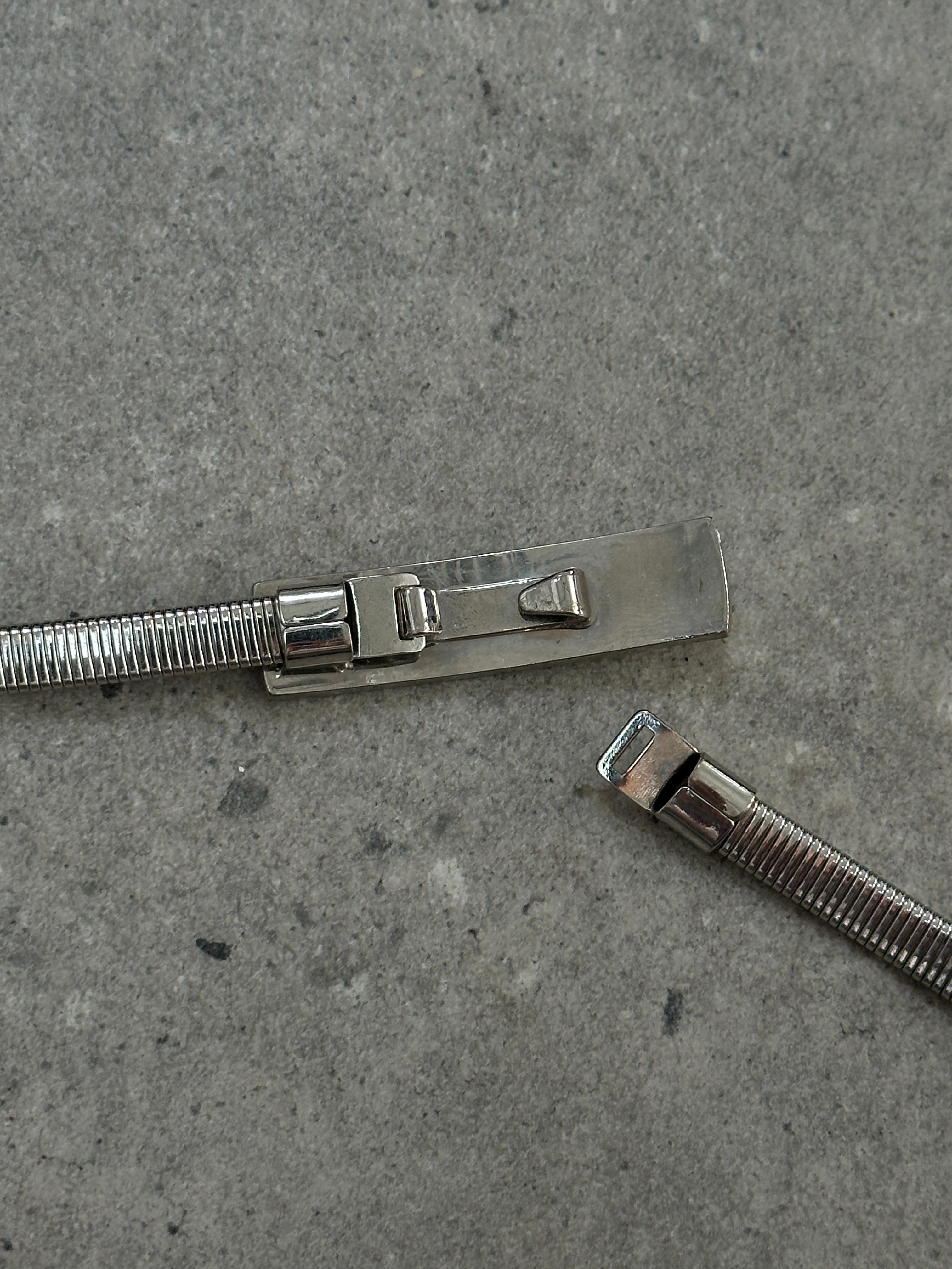 Armani Exchange stretchy metal engraved belt in silver with adjustable length from 26 to 30 inches, featuring engraved design.