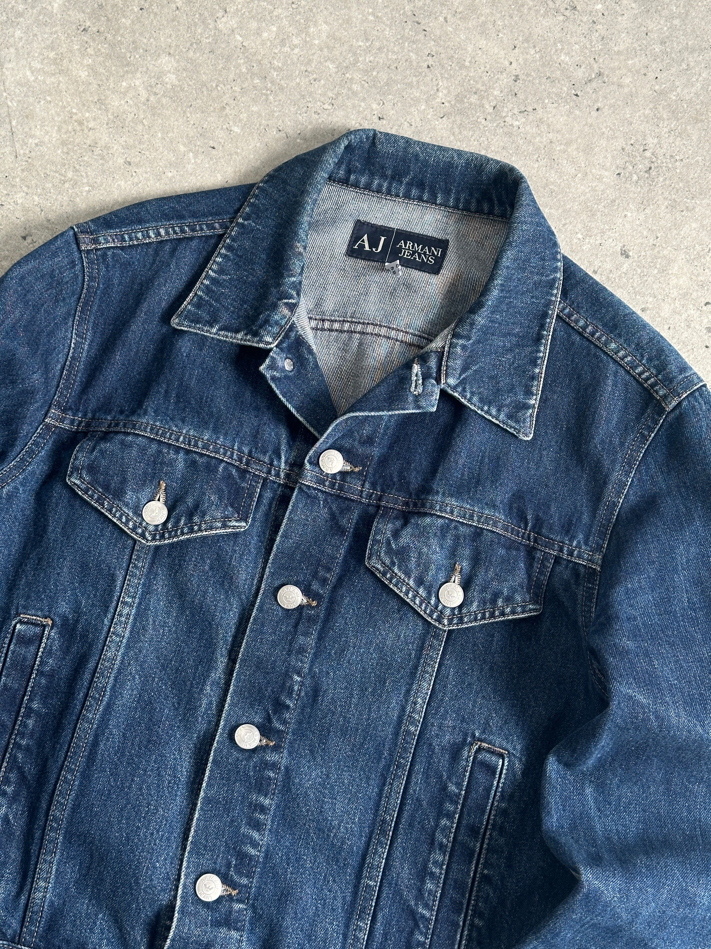 Armani Jeans mid-wash denim jacket in size S/M, featuring classic design with button-front and collar, displayed on a hanger.