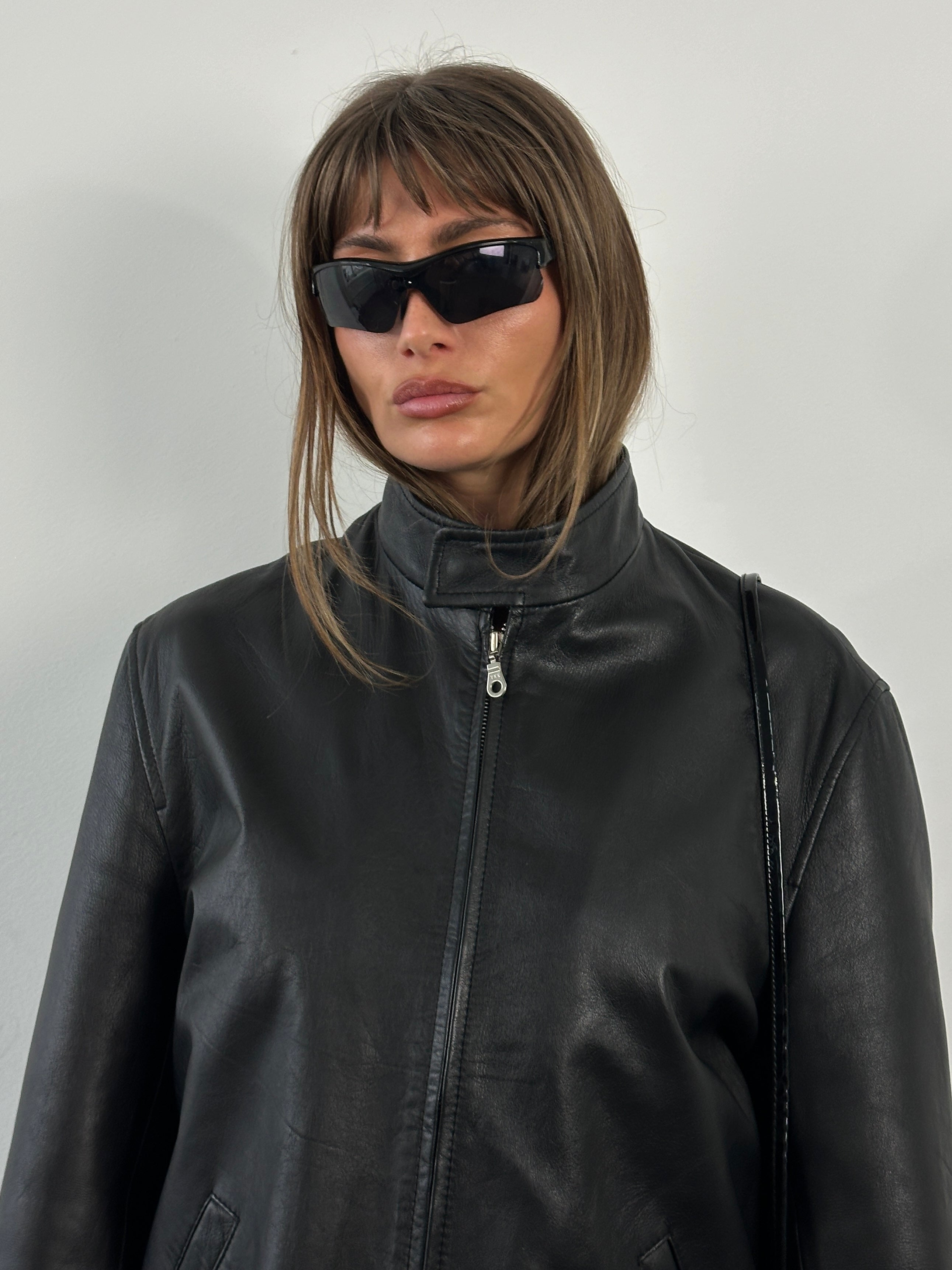 Vintage 2000s minimal high neck leather jacket in black, displayed on a hanger, featuring clean lines and a sleek design.