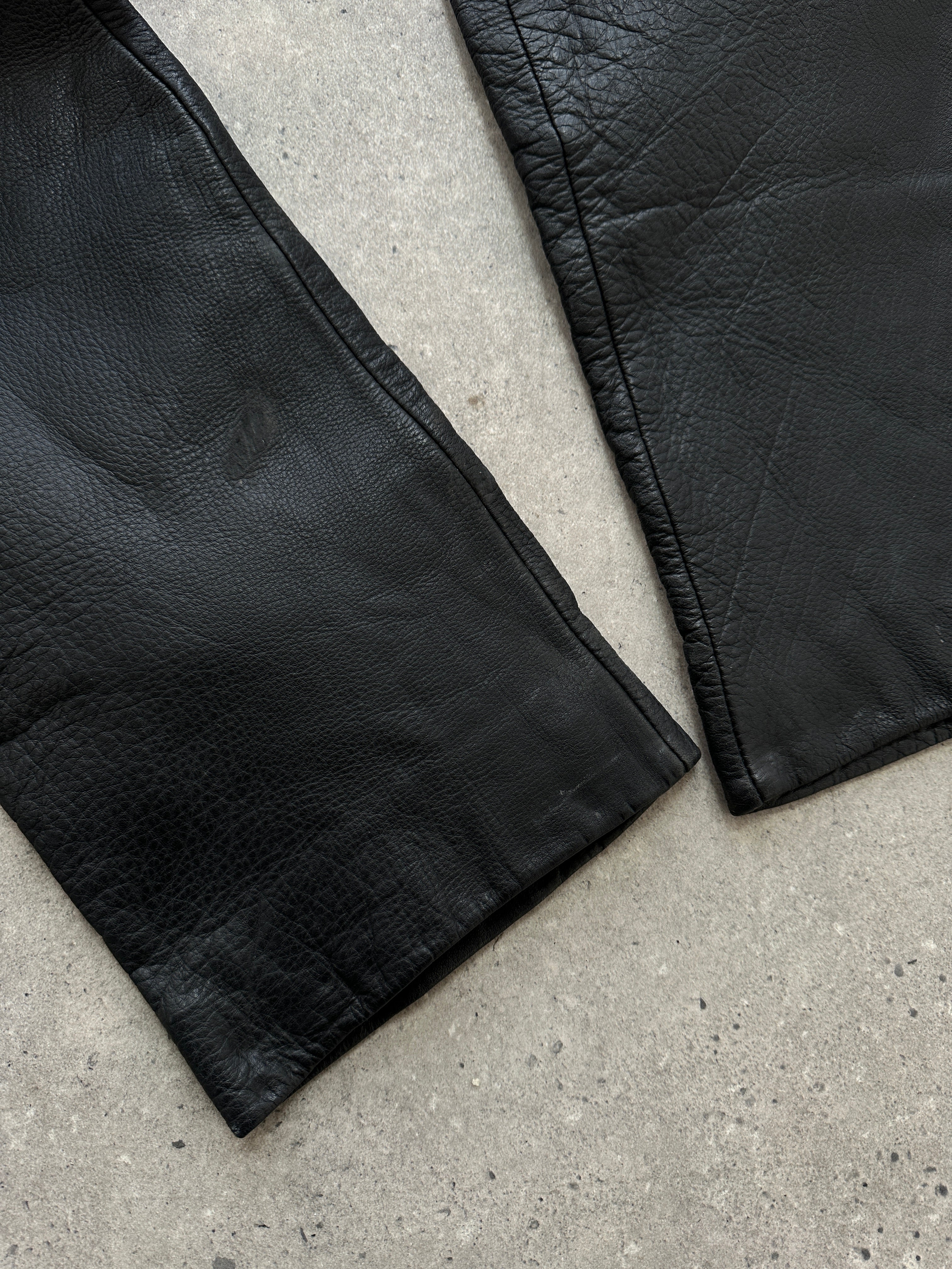 Vintage high waisted straight leg leather trousers in black with classic design, size W28, displayed on a hanger.