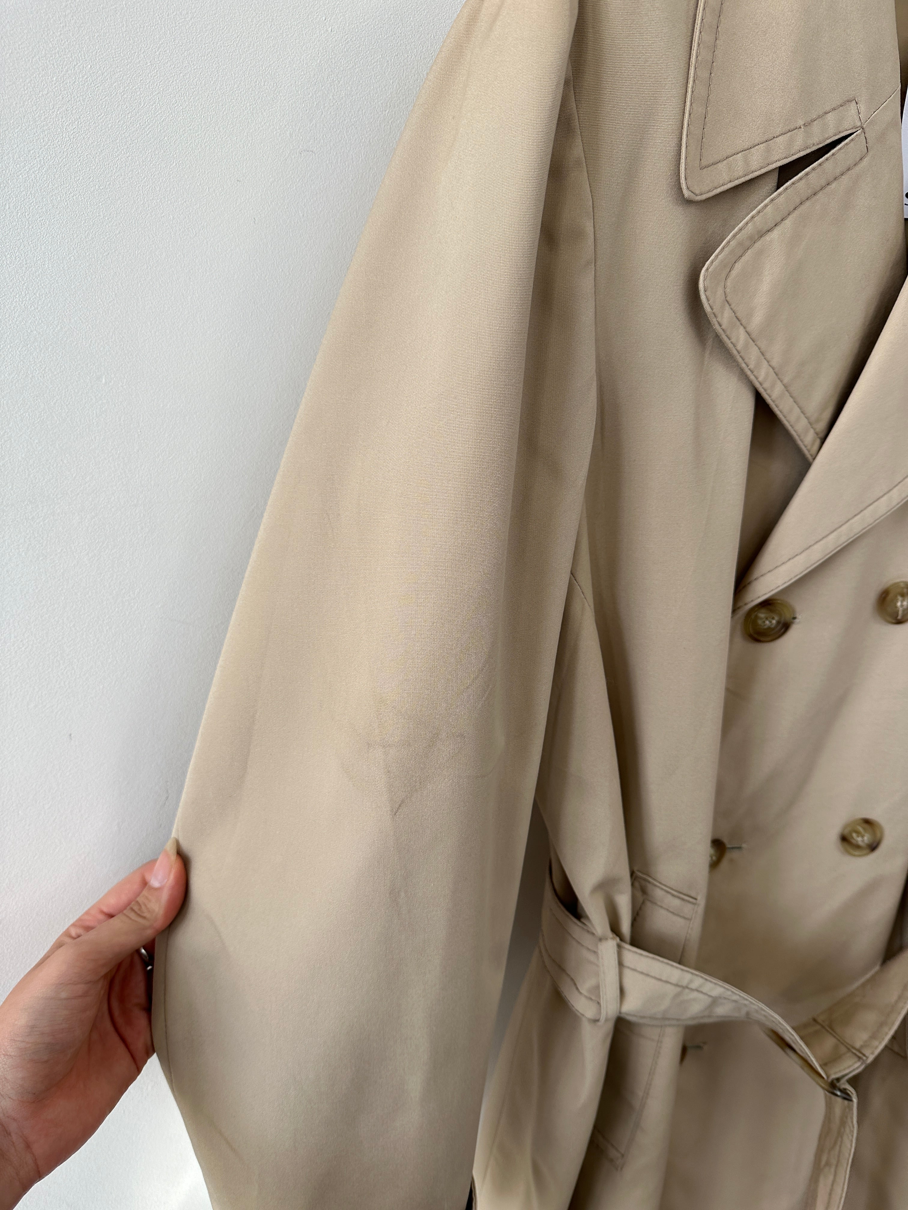 Vintage double-breasted belted trench coat in classic style, displayed on a hanger with neutral background.