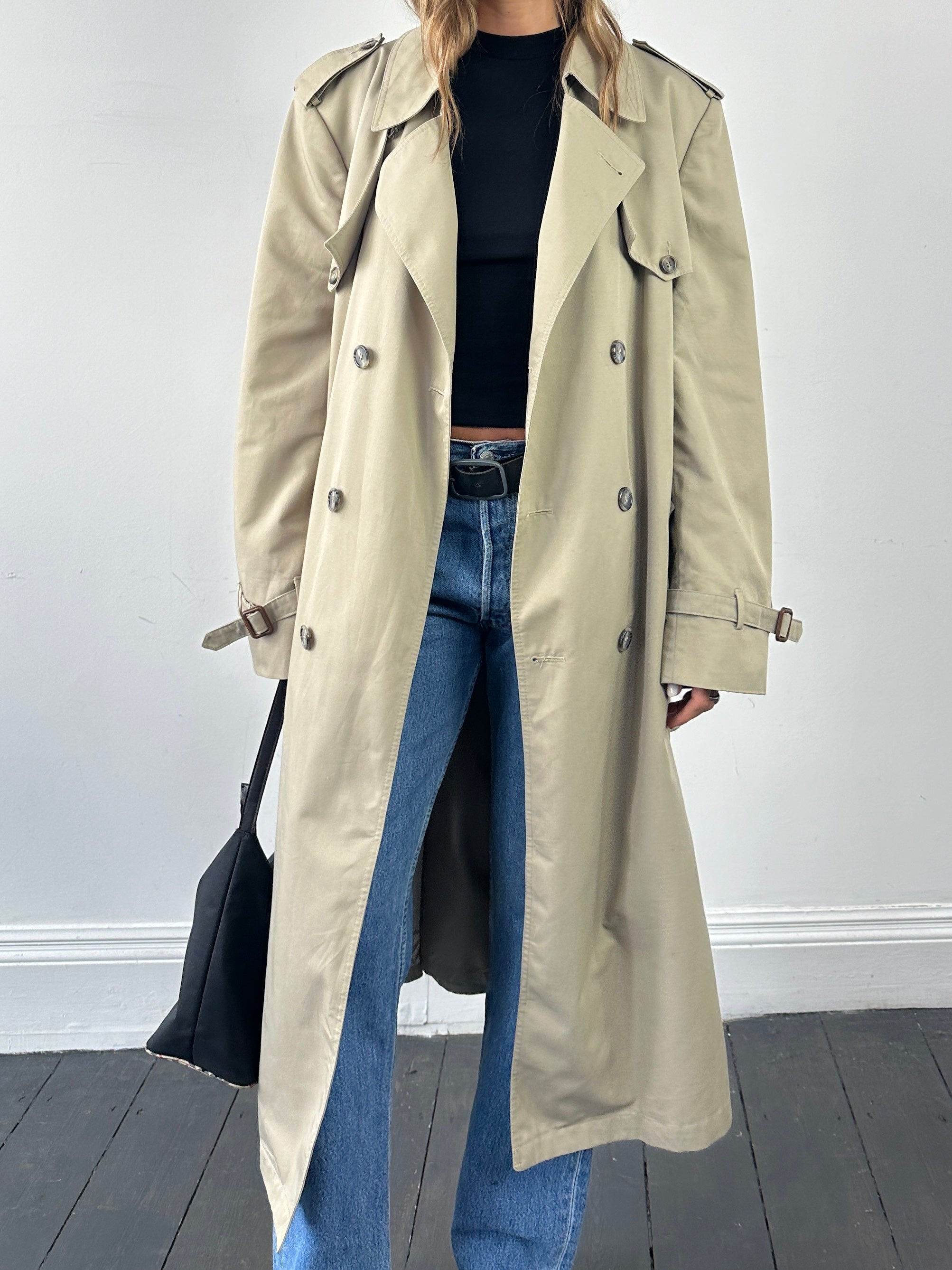 Christian Dior XL double-breasted belted trench coat displayed on a hanger, showcasing classic beige fabric and stylish design.