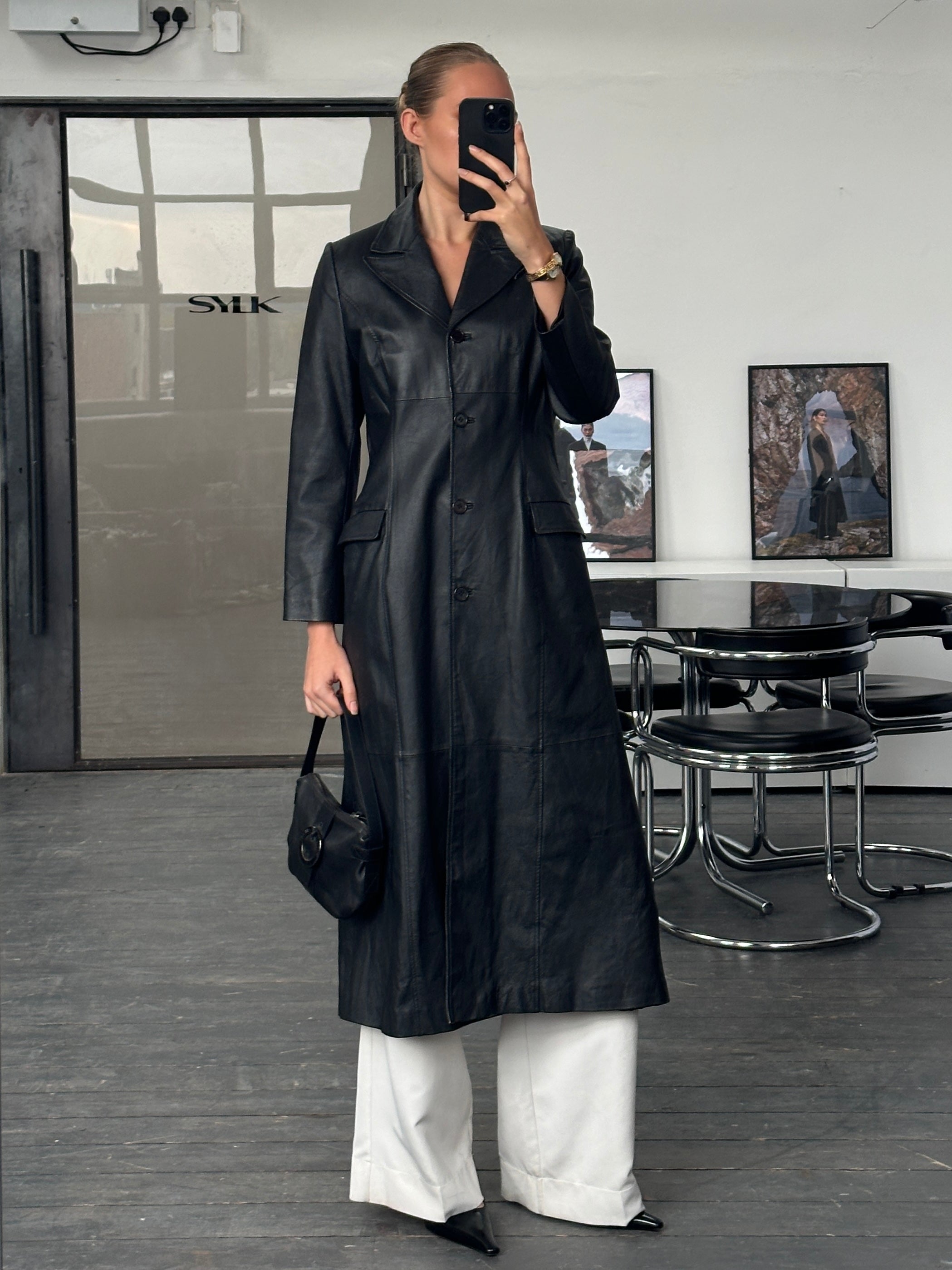 Vintage 1990s floor-length leather trench coat, black with classic collar and belt, displayed on a hanger.