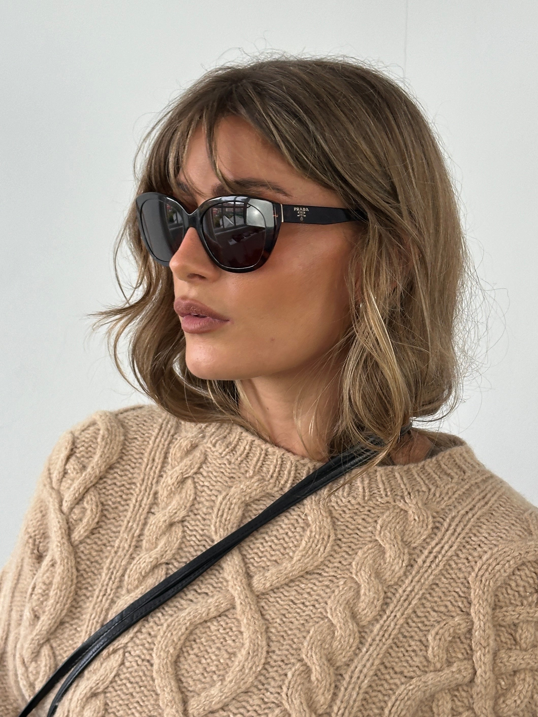 Prada tortoise shell round logo sunglasses with dark lenses and classic frame design.