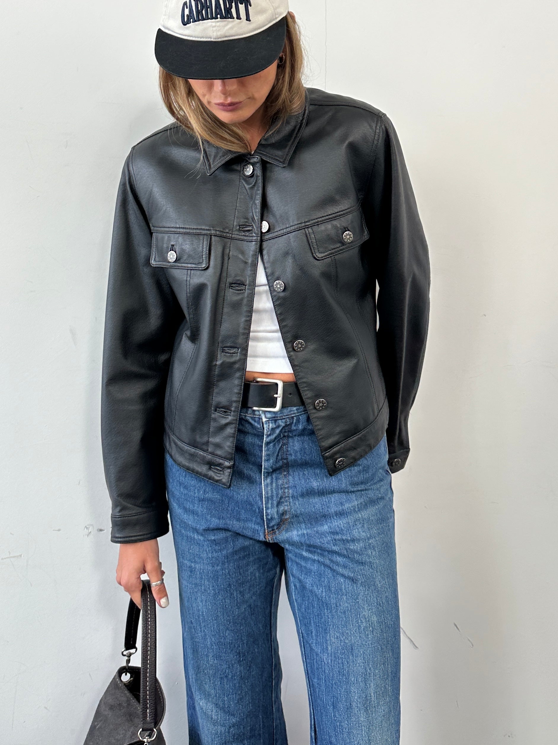 Vintage boxy leather jacket in black with front zipper and collar, displayed on a hanger. Size S/M.