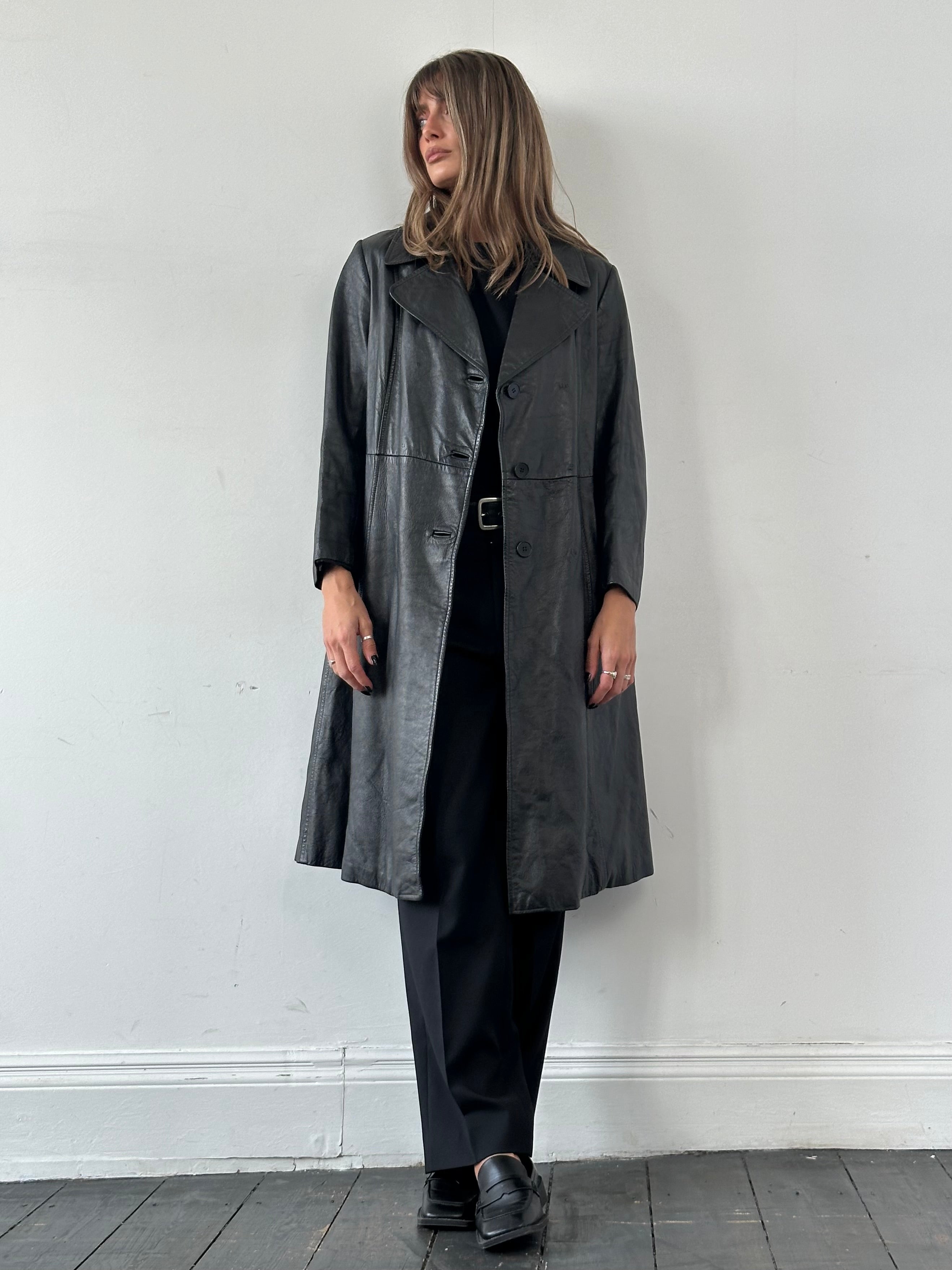 Vintage leather trench coat with belt, long sleeve, classic style, in brown leather, displayed on a hanger.
