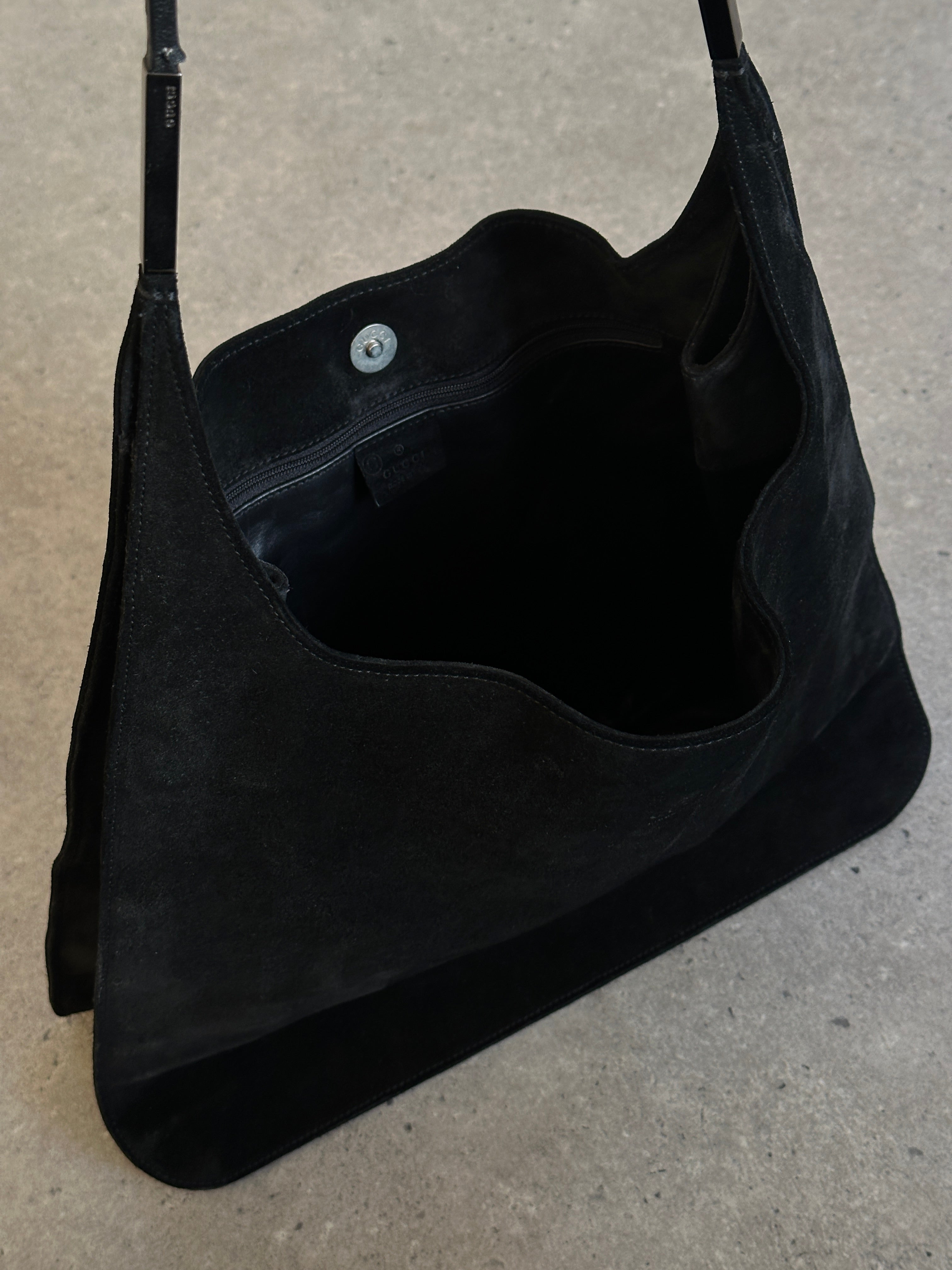 Gucci suede shoulder bag with gold hardware and adjustable strap, featuring a sleek design and signature brand logo.