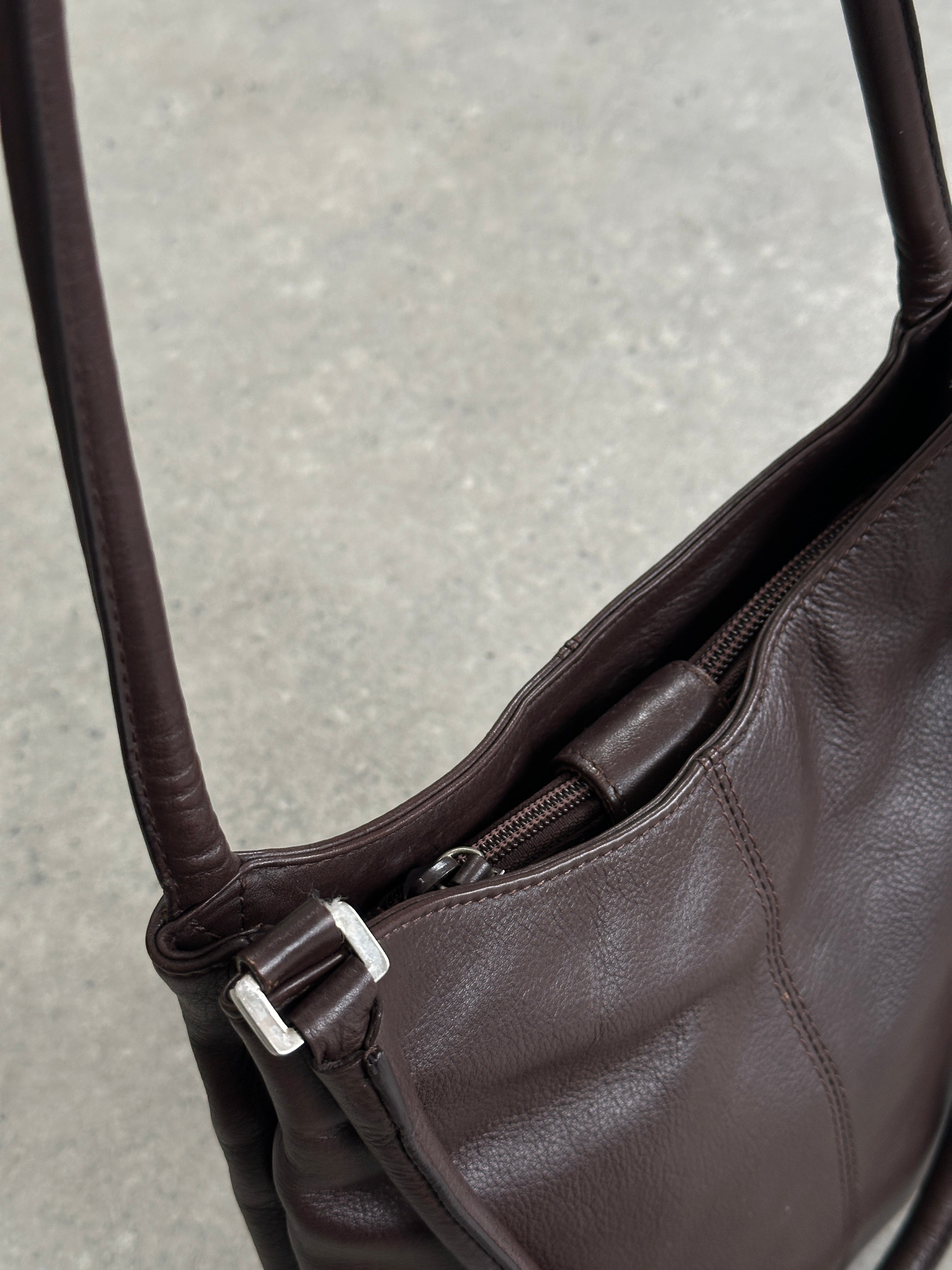 Vintage leather shoulder bag with adjustable strap, featuring a classic design and aged leather finish.