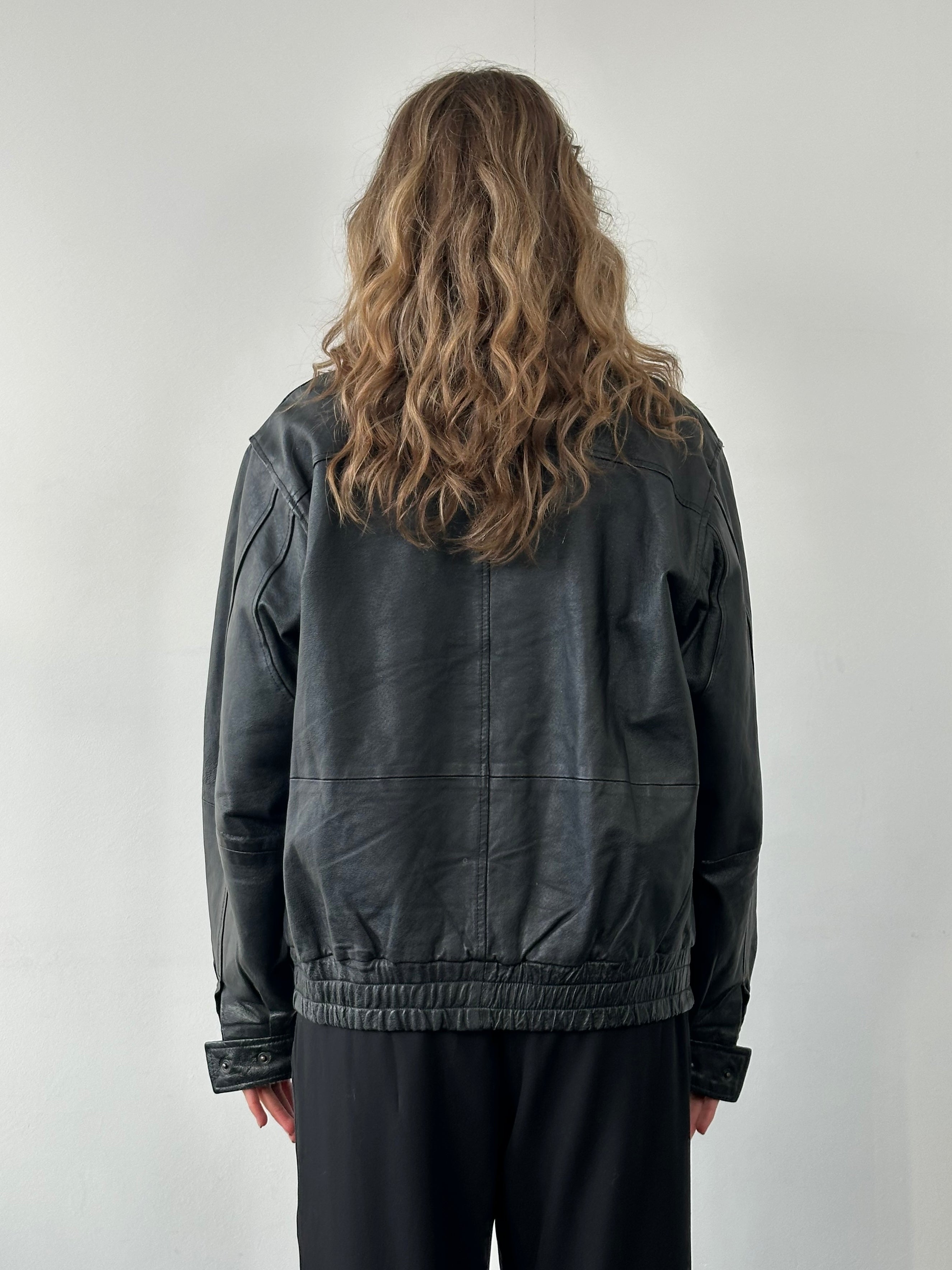 Vintage leather bomber jacket in size M/L, featuring classic design with ribbed cuffs and collar, displayed on a hanger.