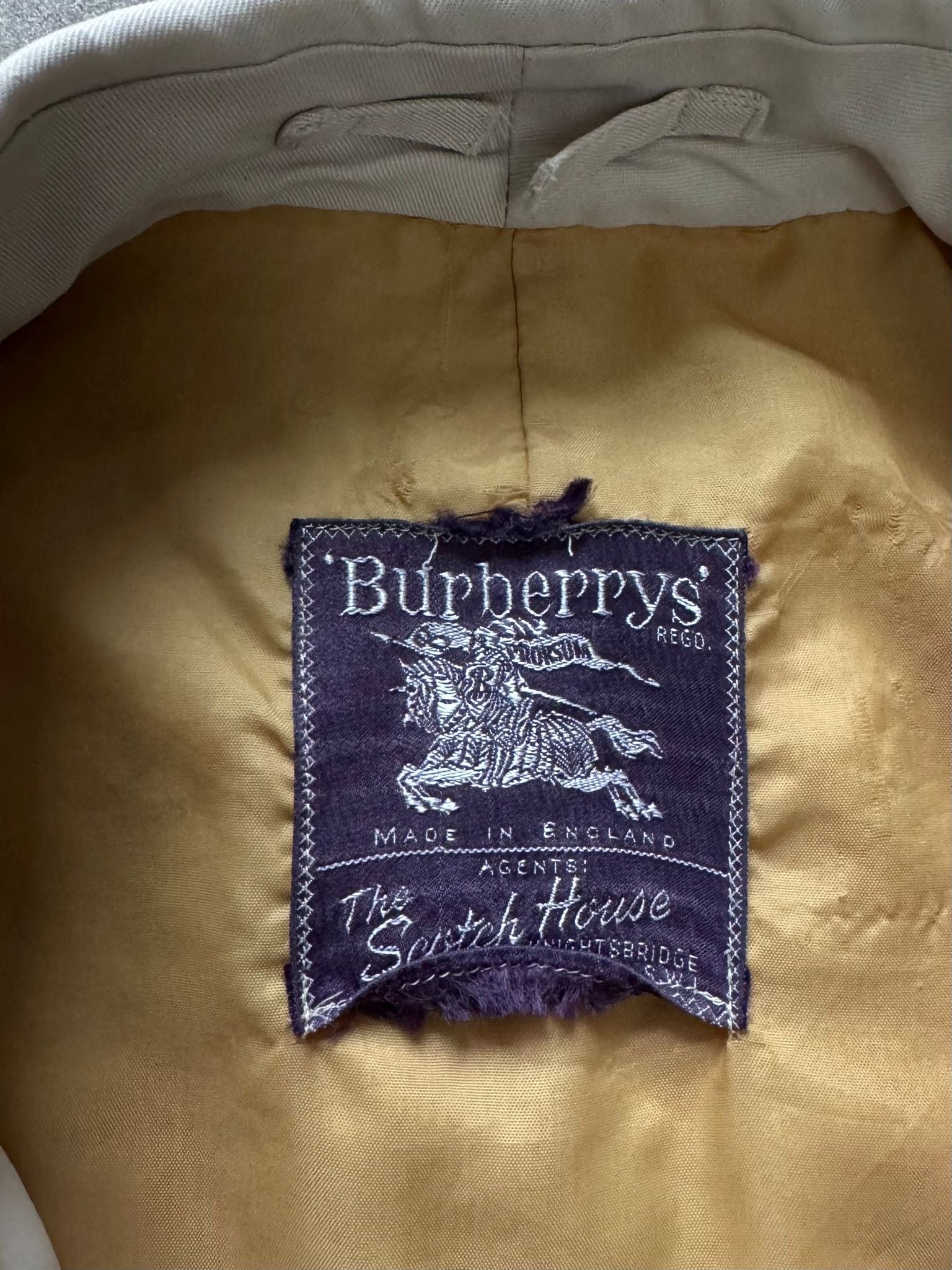 Burberry 1990s cotton double-breasted trench coat in beige with classic belt and button details, displayed on a hanger.