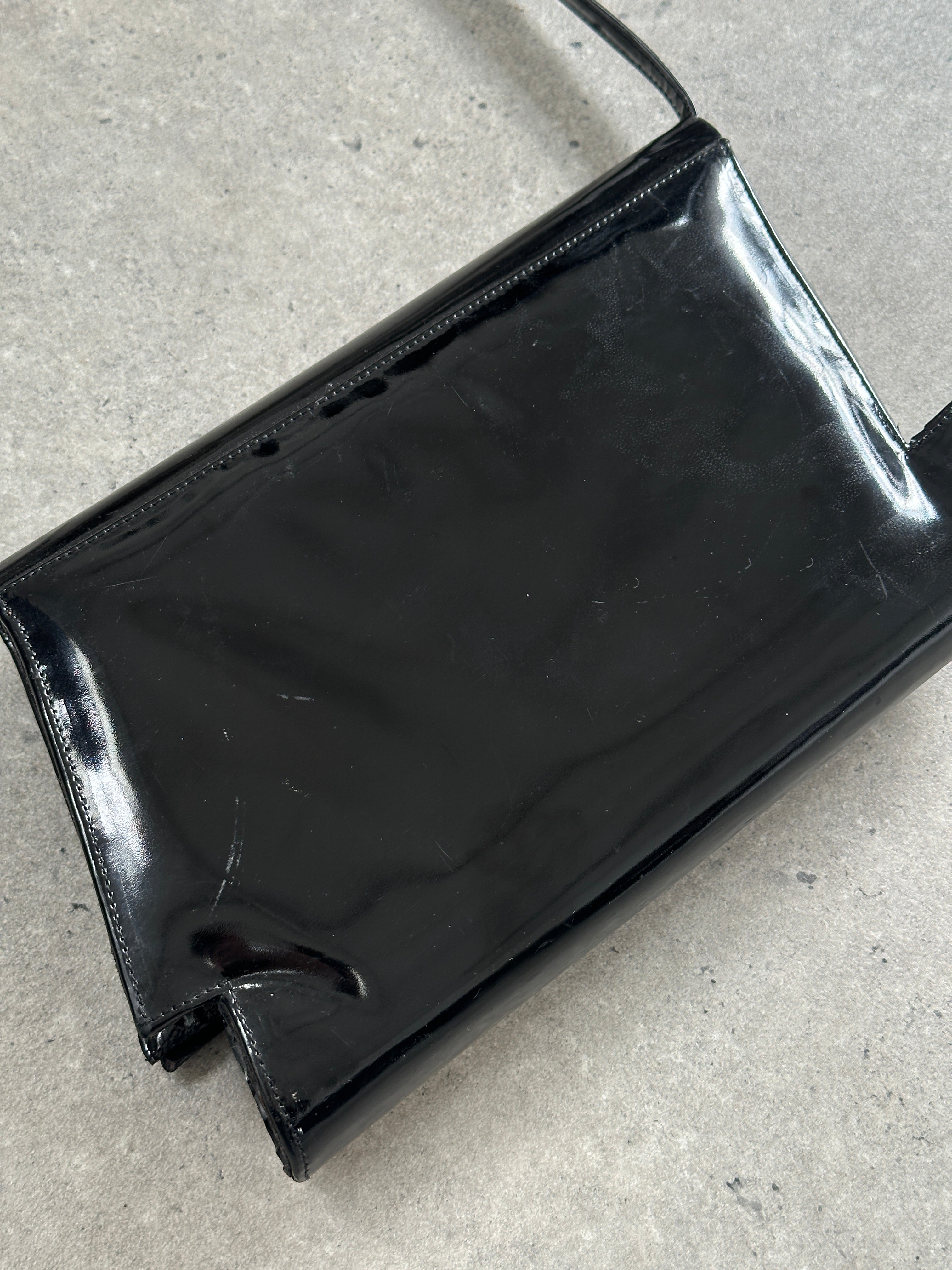 Charles Jourdan 1990s asymmetric patent crossbody bag with sleek design and structured silhouette, black glossy finish, and adjustable strap.