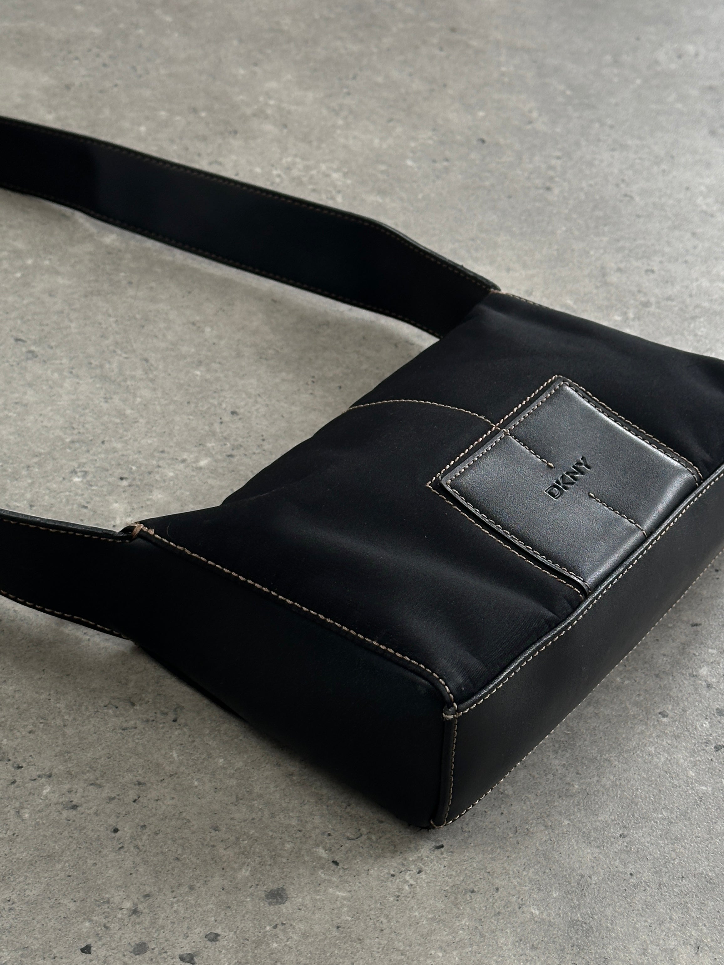 Black DKNY contrast stitch crossbody bag with adjustable strap and sleek design, perfect for everyday use.