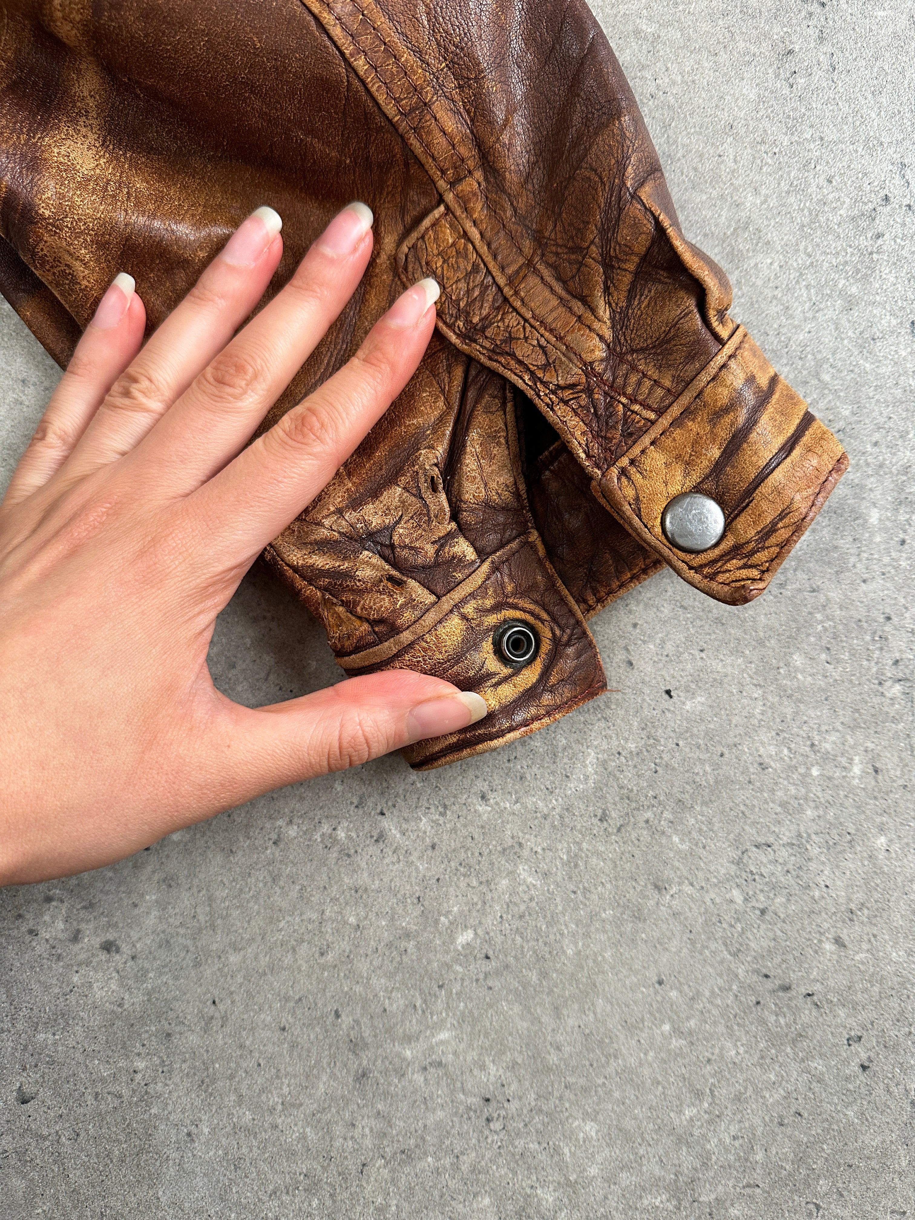 Vintage 1990s aged leather bomber jacket in XL size, featuring distressed brown leather and classic ribbed cuffs.