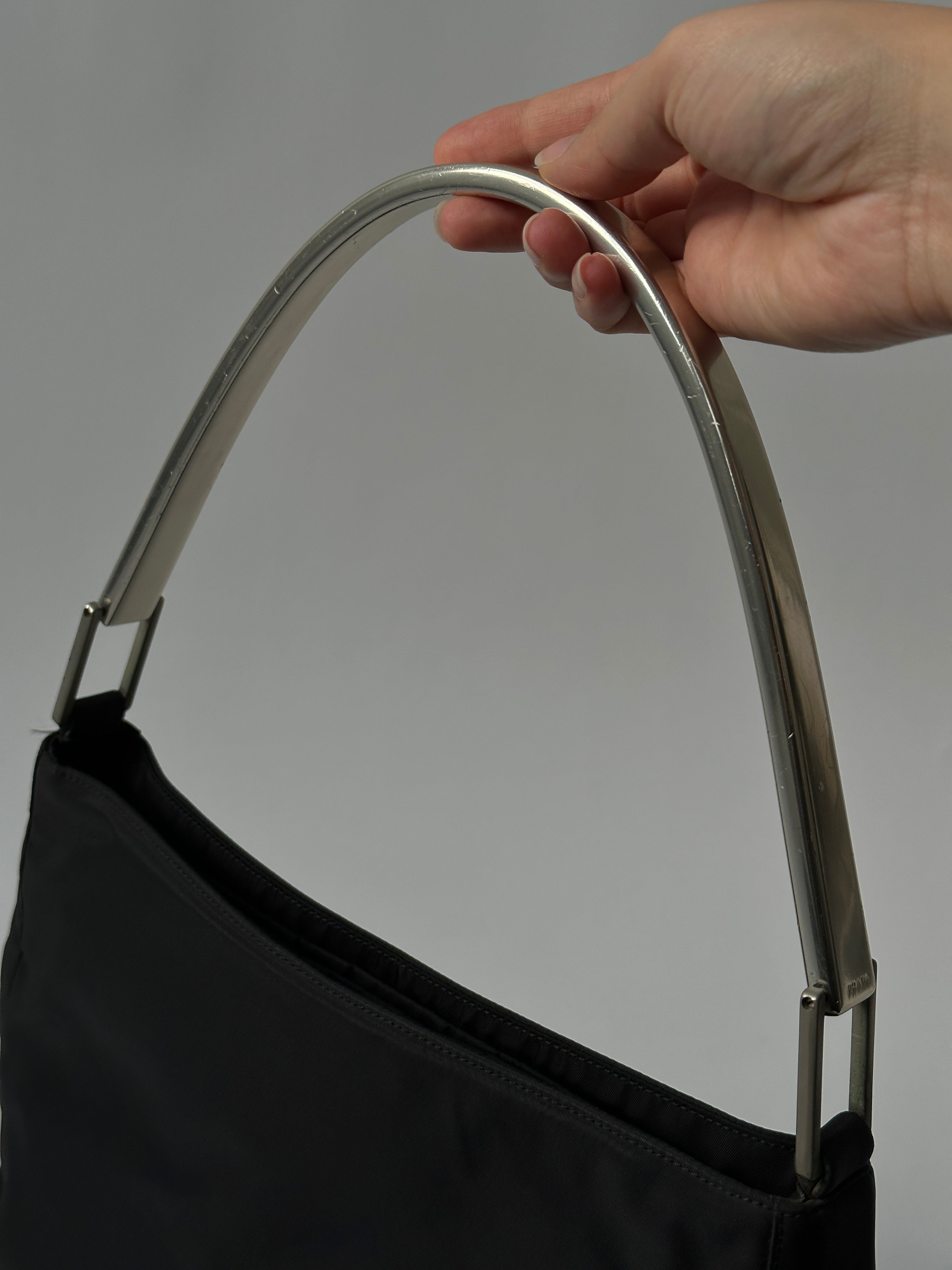 Prada nylon shoulder bag with metal handle, featuring sleek design and durable nylon material.