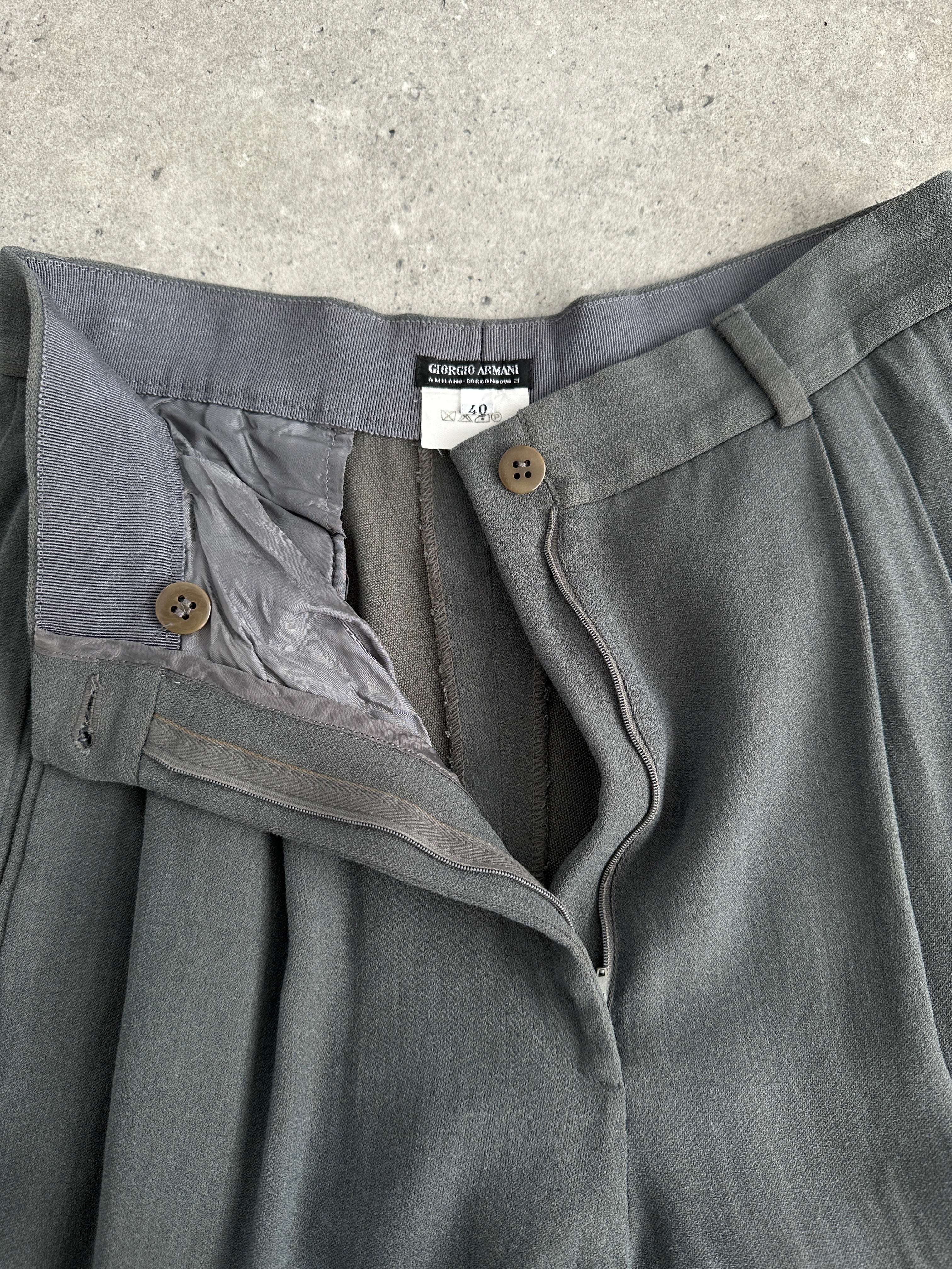 Giorgio Armani high-waisted tapered leg pleated trousers in neutral fabric, displayed on a hanger with a clean background.