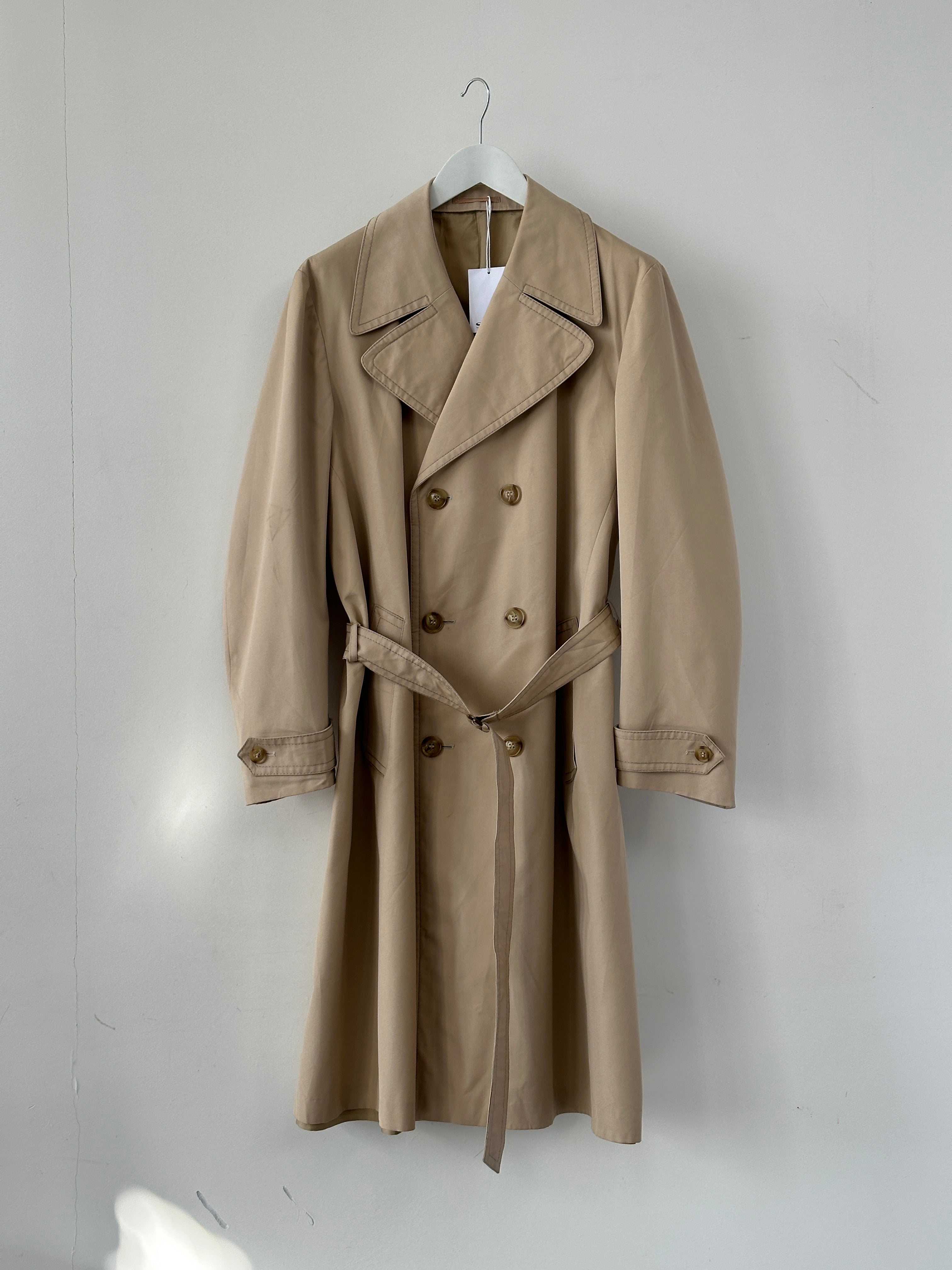 Vintage double-breasted belted trench coat in classic style, displayed on a hanger with detailed collar and belted waist.