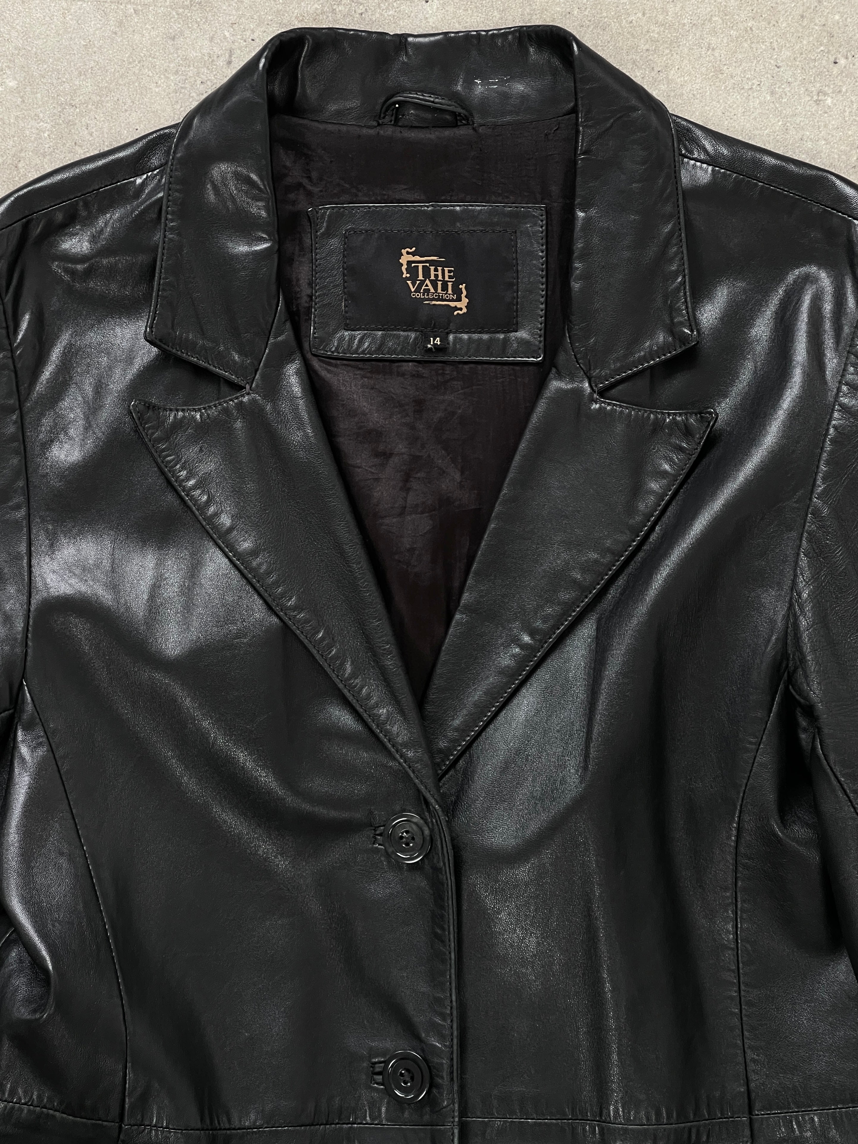 Vintage 1990s leather trench coat, floor-length style, in black leather, displayed on a hanger with classic design details.
