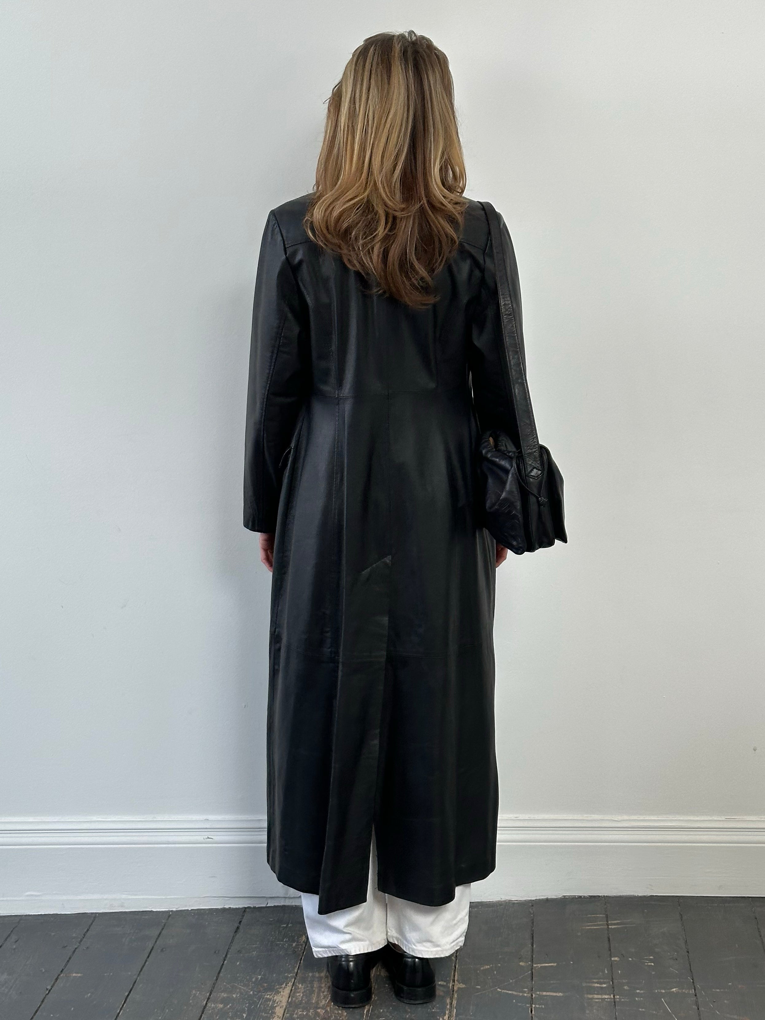 Vintage 1980s leather trench coat, floor length, medium size, shown hanging with classic design and rich brown leather texture.