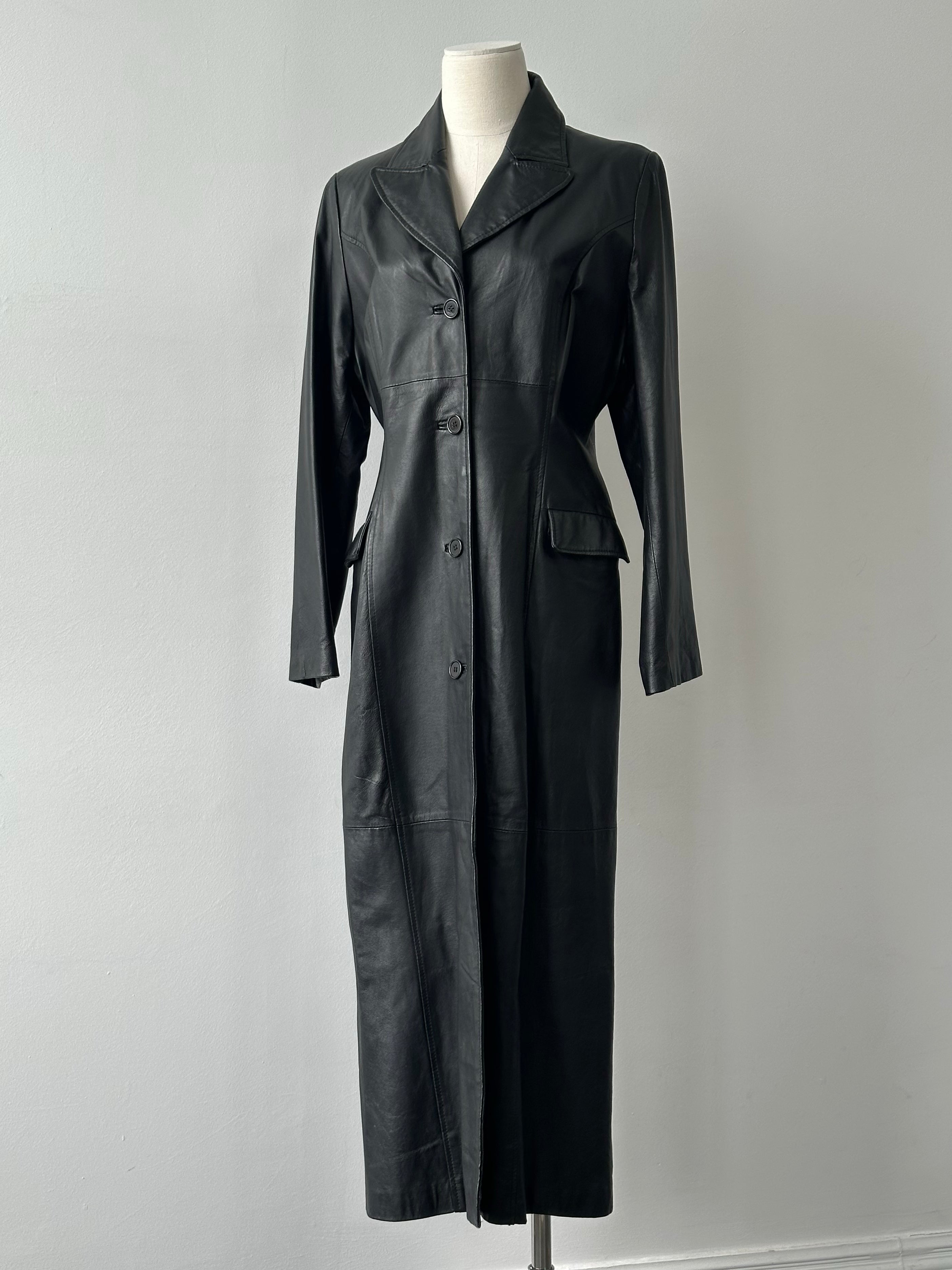 Vintage 1980s leather trench coat, full-length, in a classic design with a collar and button details, displayed on a hanger.