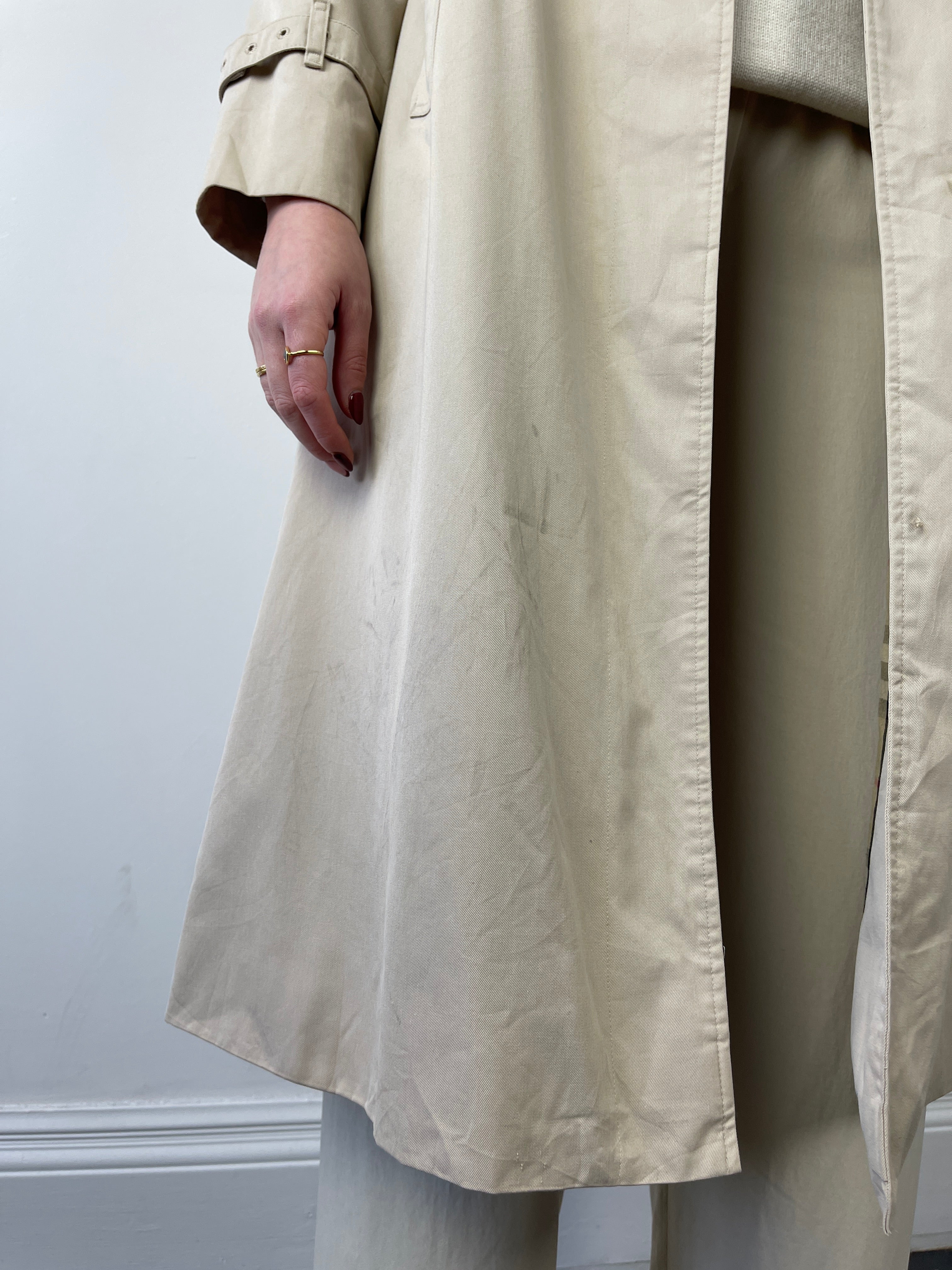 Beige Burberry trench coat displayed on a hanger, showcasing classic design and signature check lining inside.