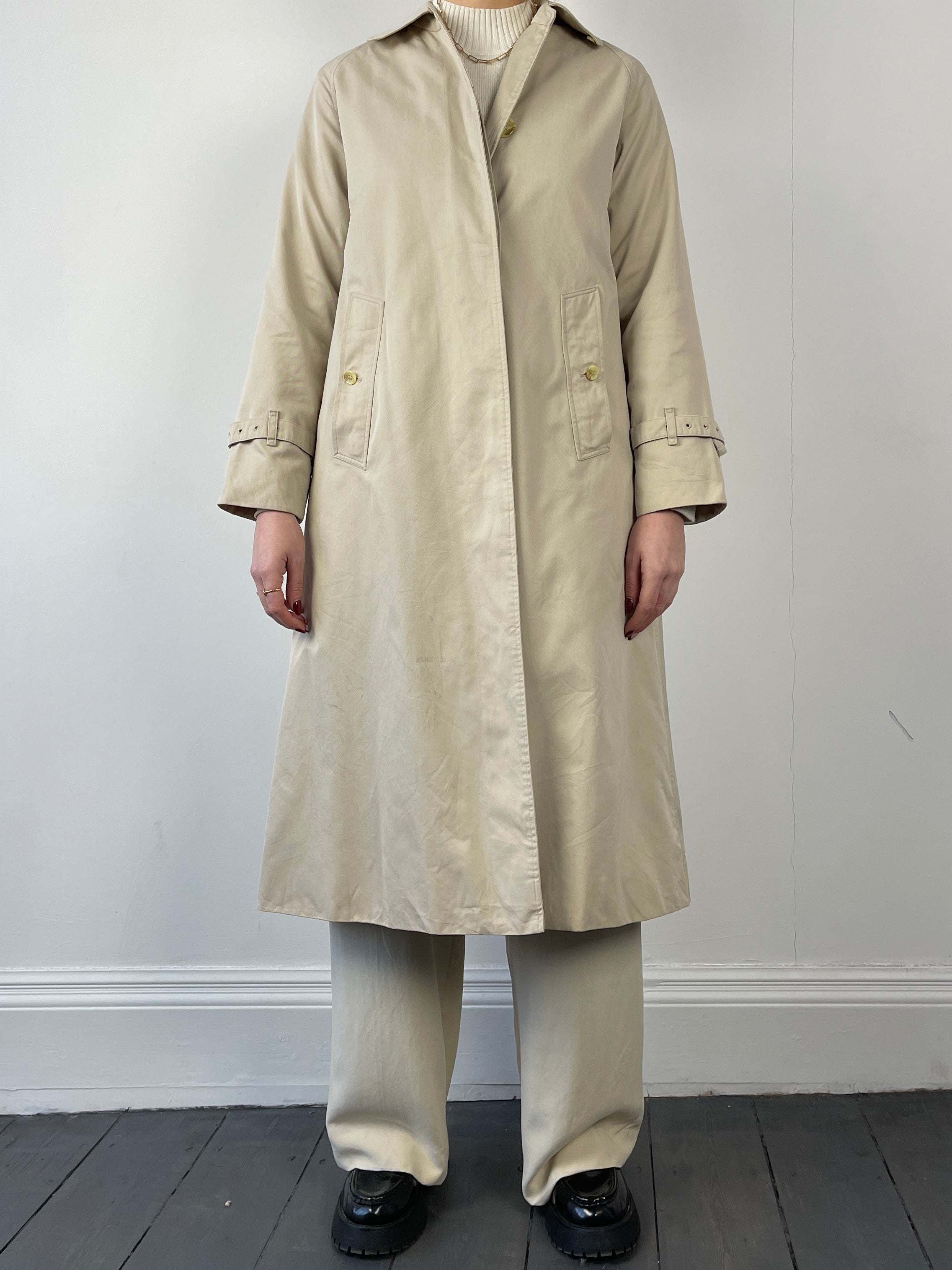 Beige Burberry trench coat with classic double-breasted design and belt, shown on a mannequin.