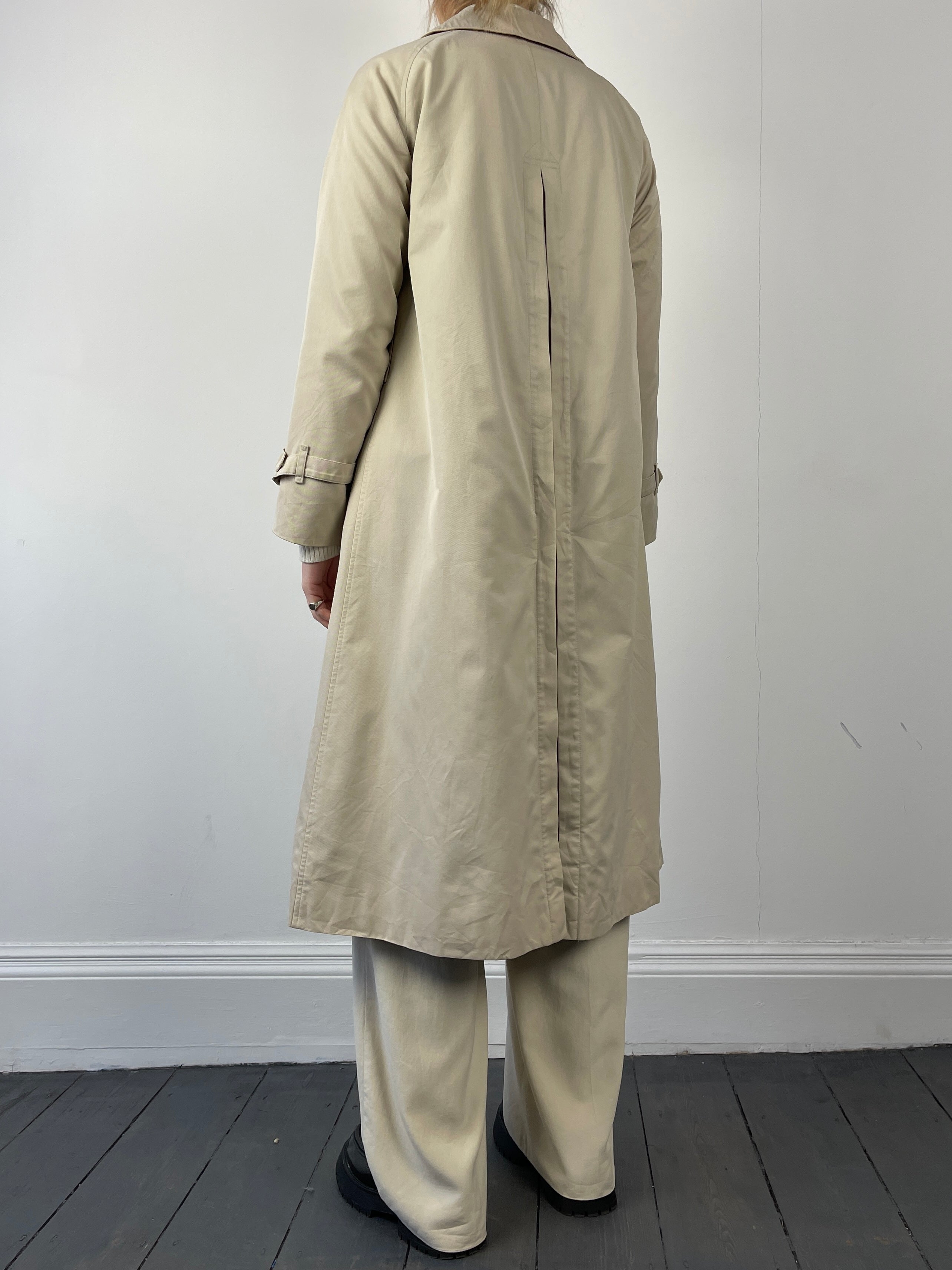 Beige Burberry trench coat displayed on a hanger, featuring classic double-breasted design and adjustable waist belt.
