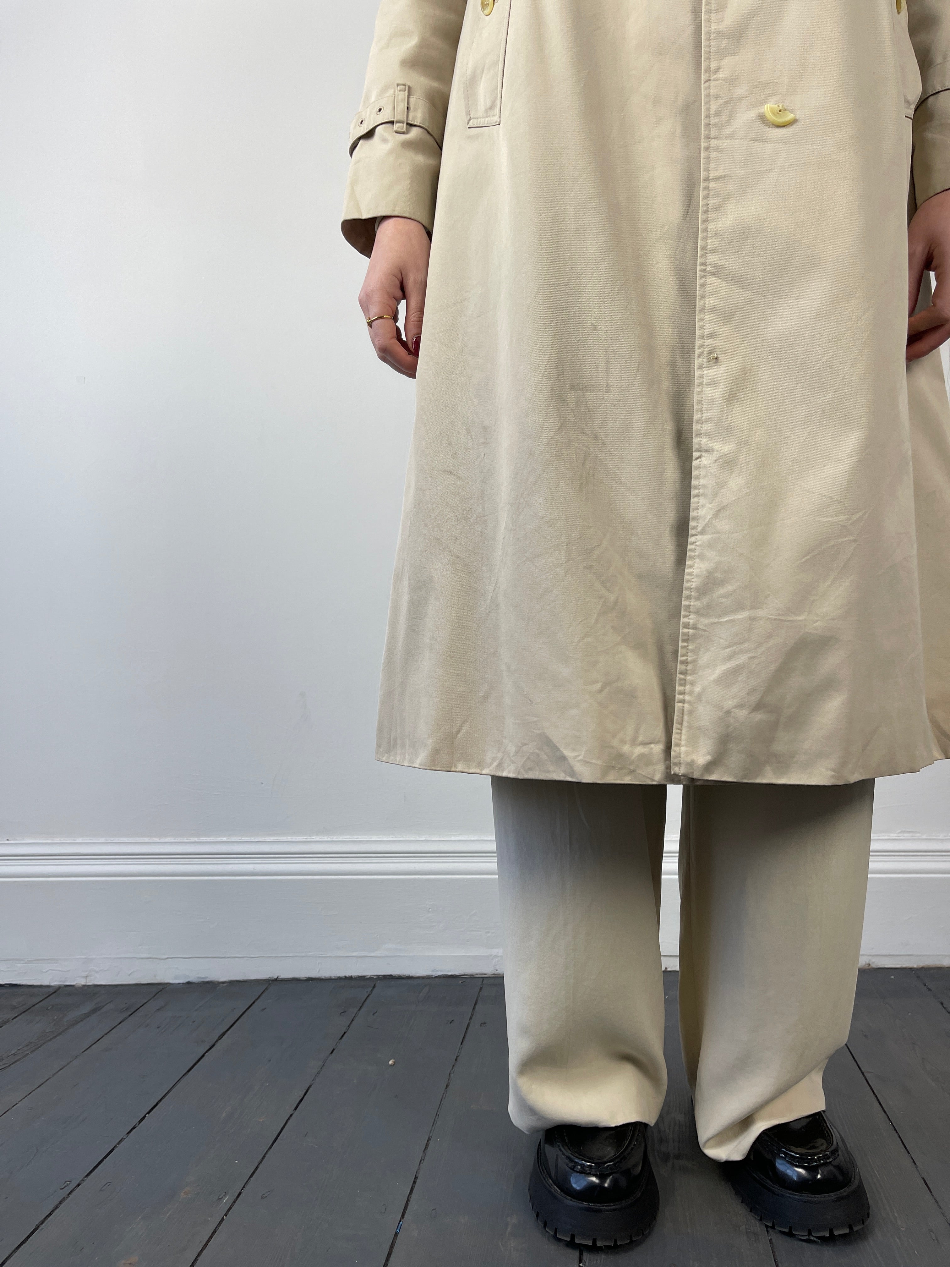 Beige Burberry trench coat displayed on a hanger, showcasing classic double-breasted design and signature check lining.