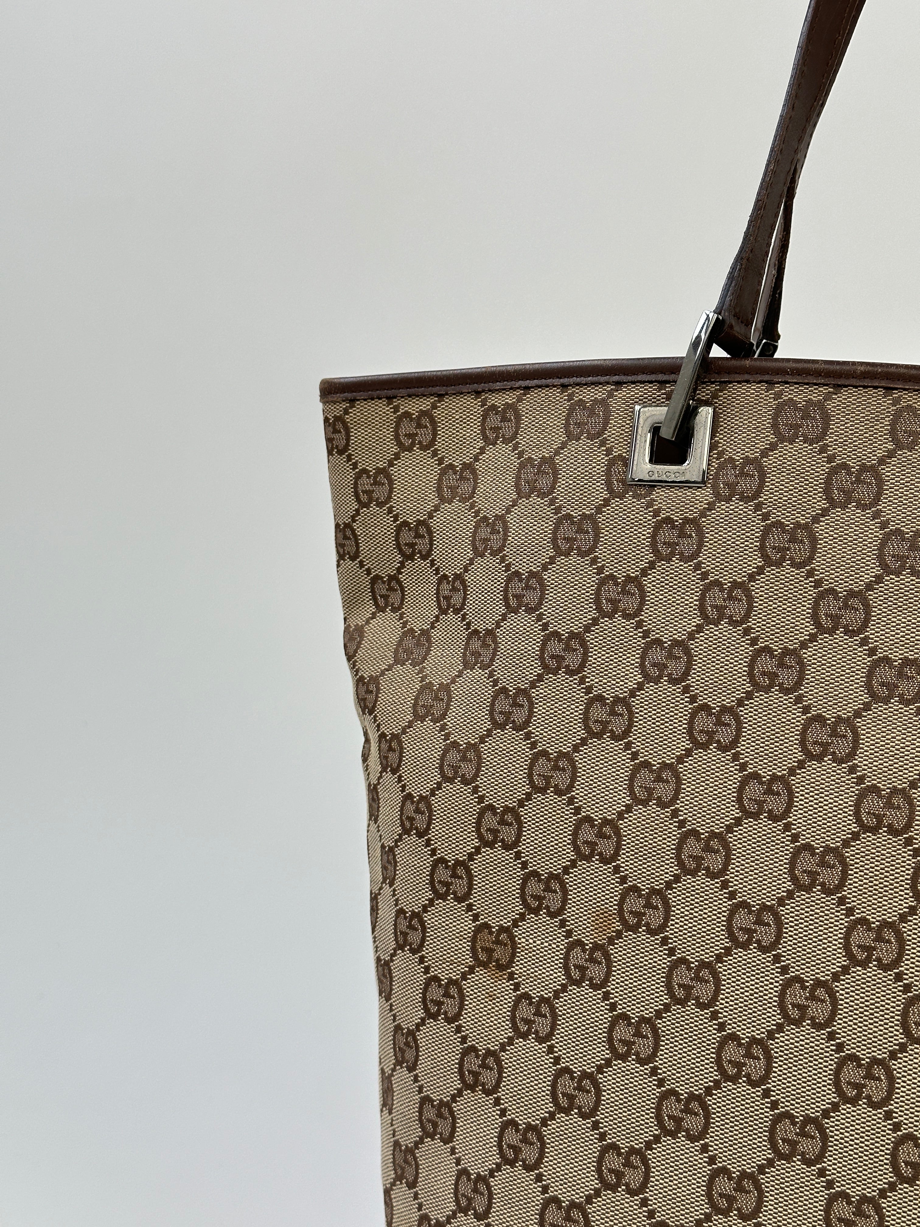Gucci Monogram GG bucket tote bag with leather trim and adjustable shoulder strap, featuring signature monogram pattern and spacious interior.