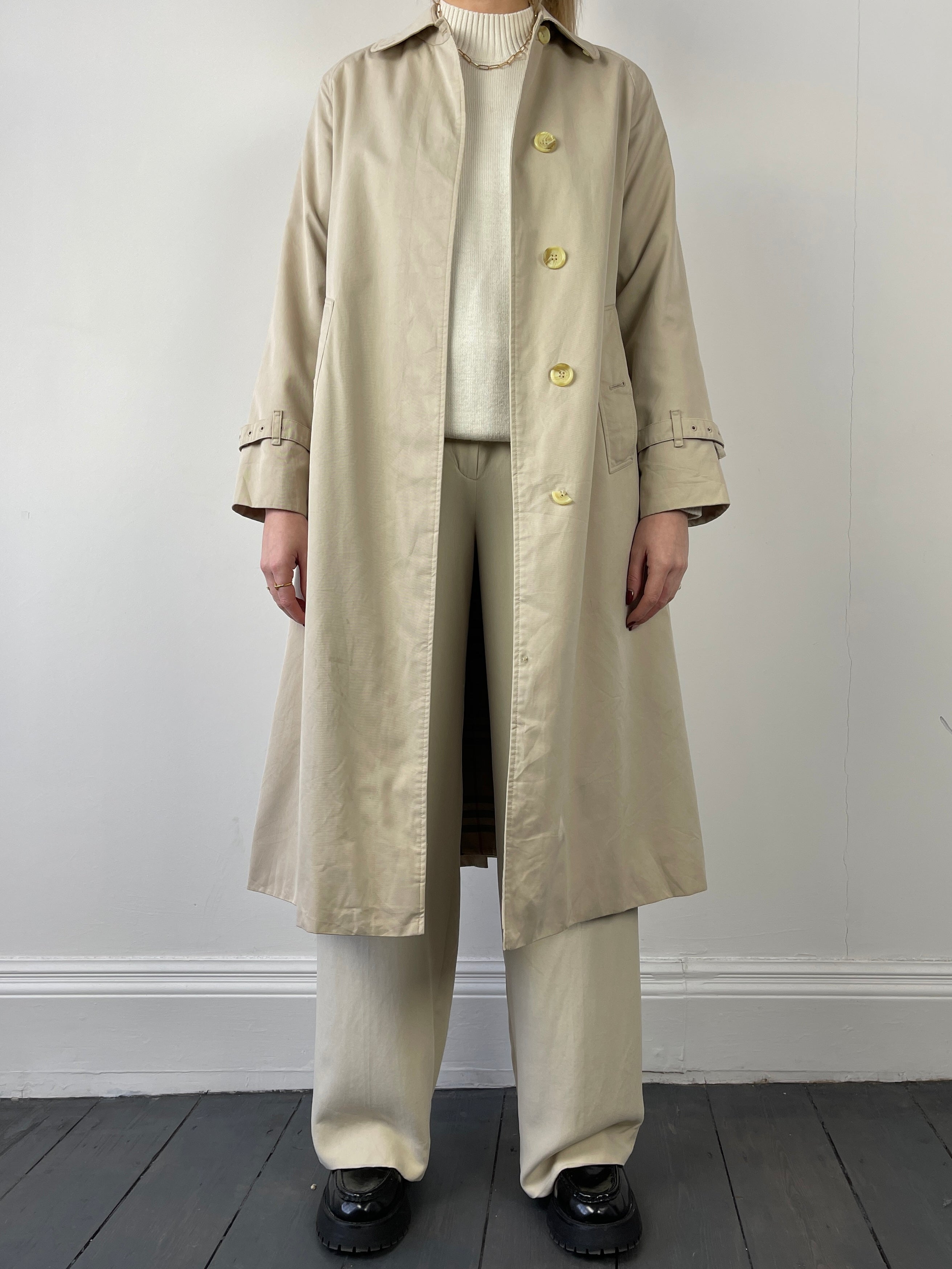 Burberry trench coat displayed on a hanger, featuring classic beige fabric, double-breasted design, and signature Burberry check lining.