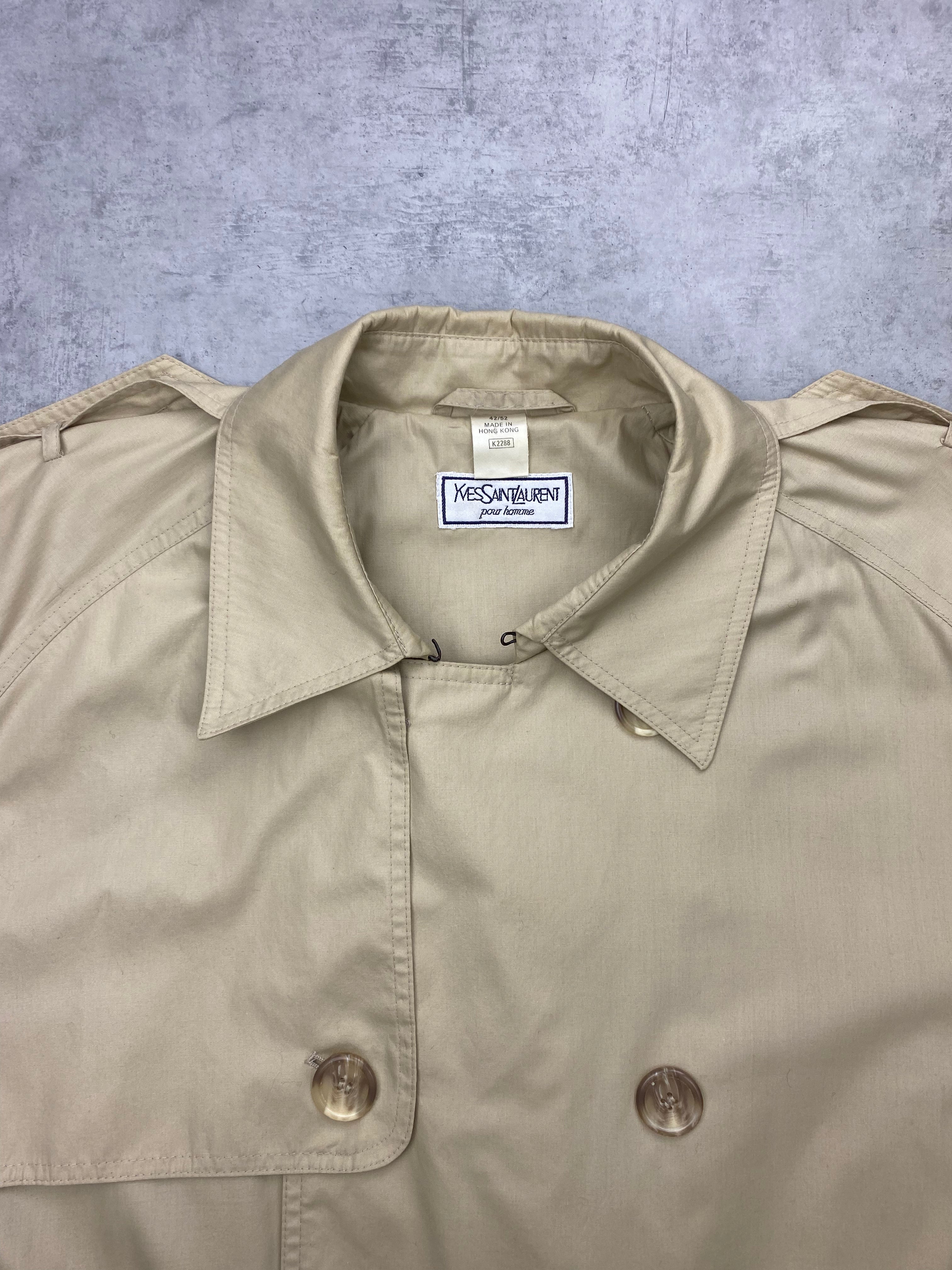 Yves Saint Laurent cotton trench coat displayed on a hanger, showcasing classic double-breasted design and neutral beige color.