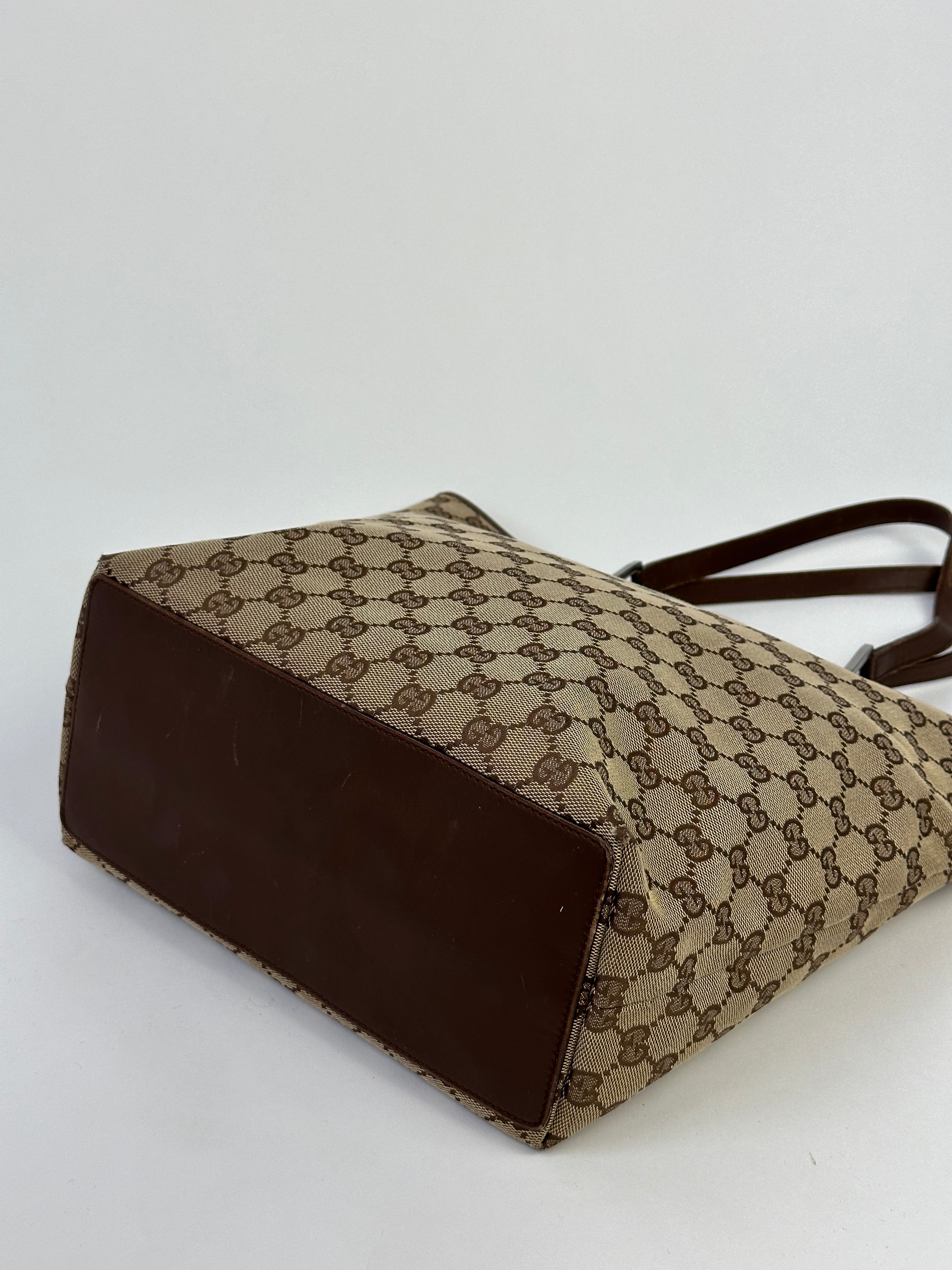 Gucci Monogram GG bucket tote bag with beige canvas and leather trim, featuring signature Gucci pattern and sturdy handles.