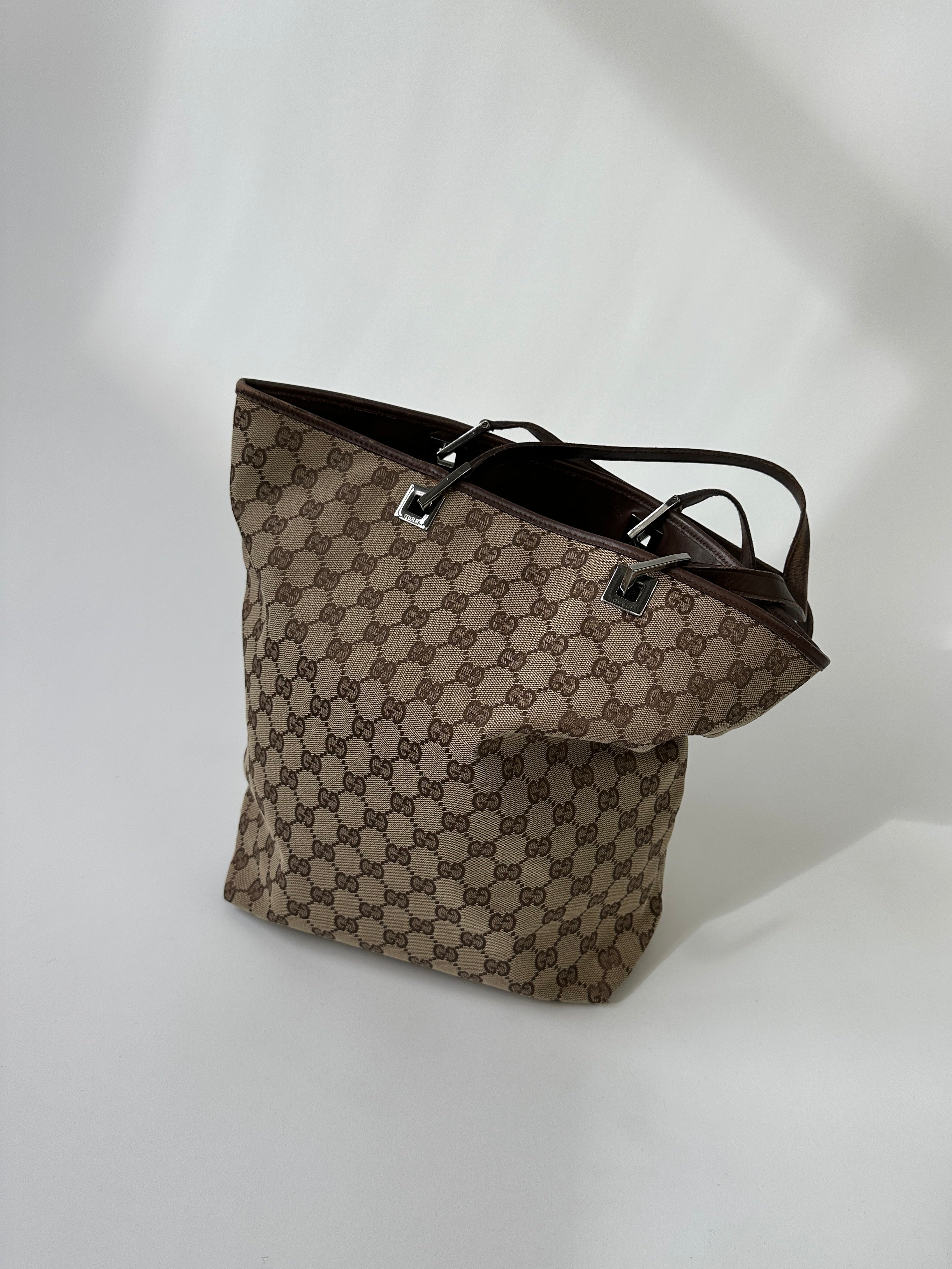 Gucci Monogram GG bucket tote bag with leather trim and adjustable strap, featuring the iconic Gucci monogram pattern.