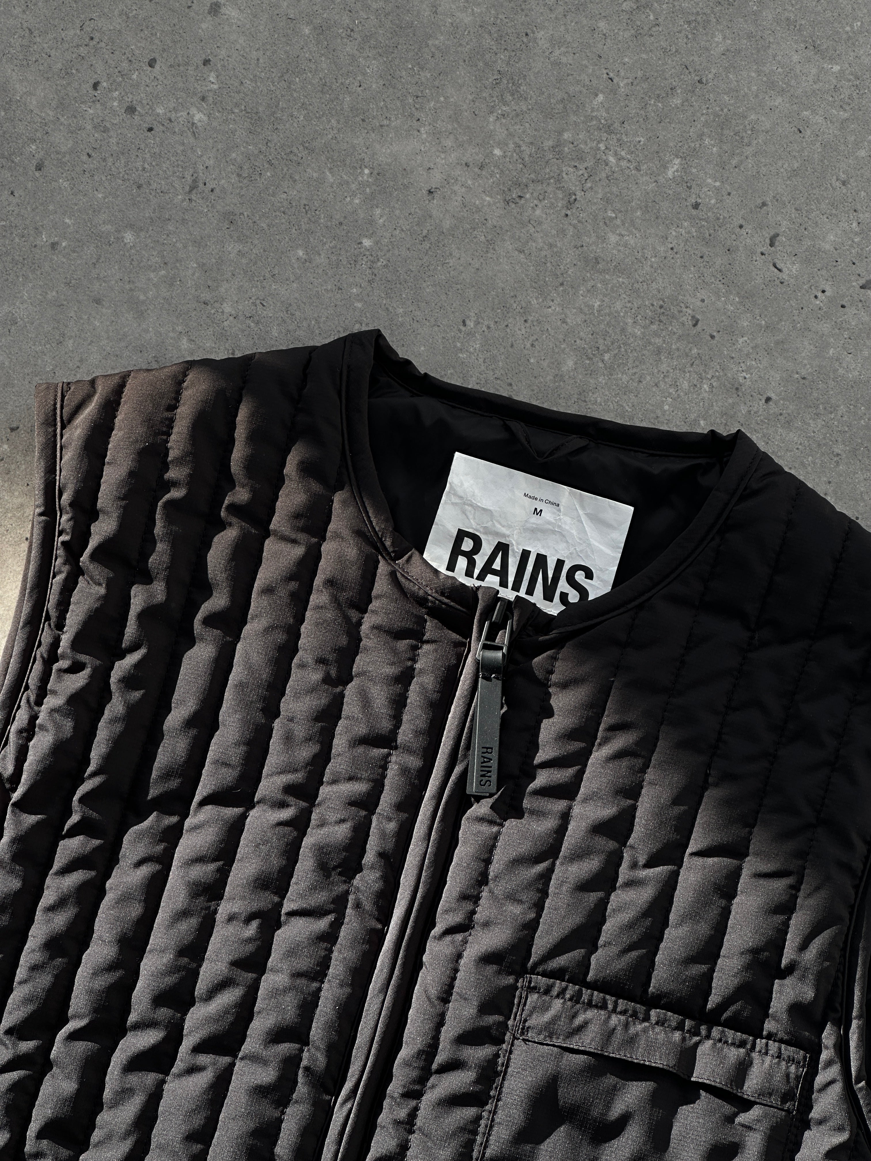 Rains waterproof zip-up liner vest gilet in black, showing the front view with a high collar and sleek design.