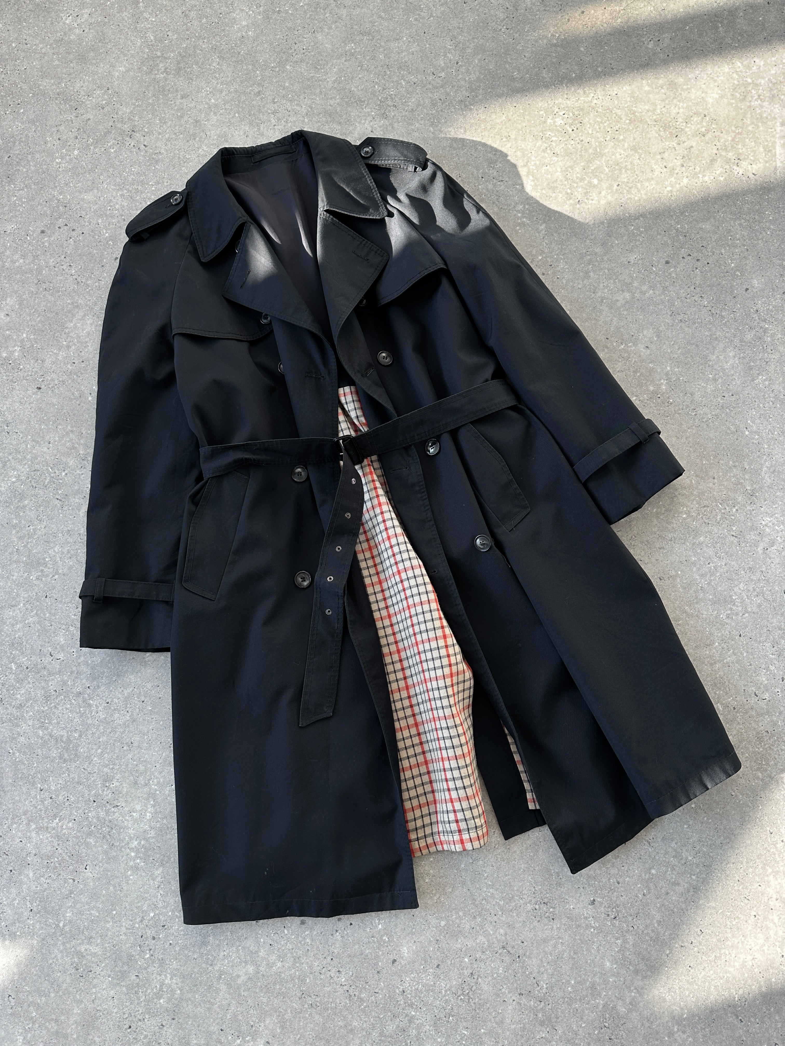 Black vintage belted cotton trench coat with large lapels and classic design, displayed on a hanger.