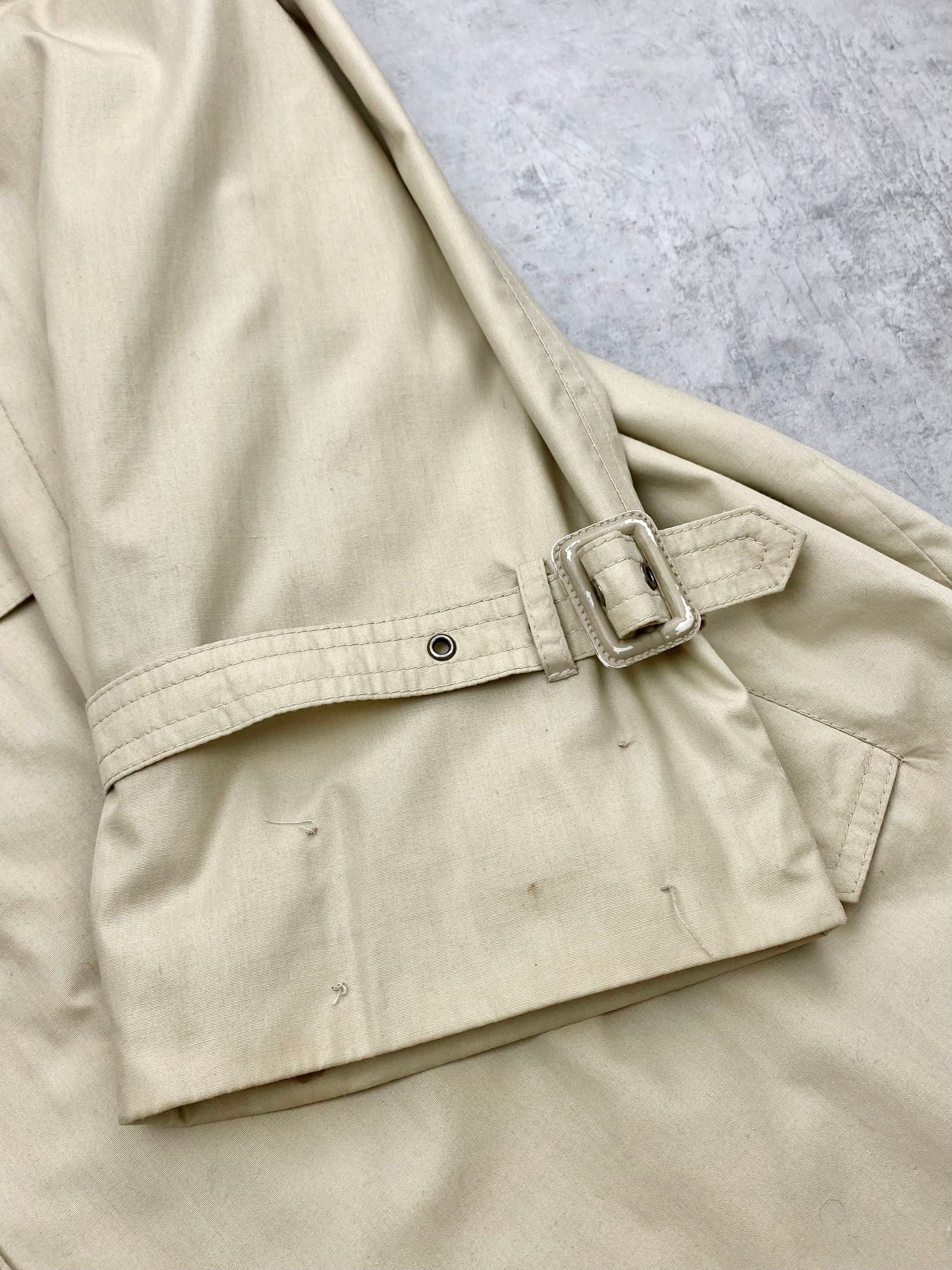Beige Yves Saint Laurent cotton trench coat with classic double-breasted design and belt, displayed on a hanger.